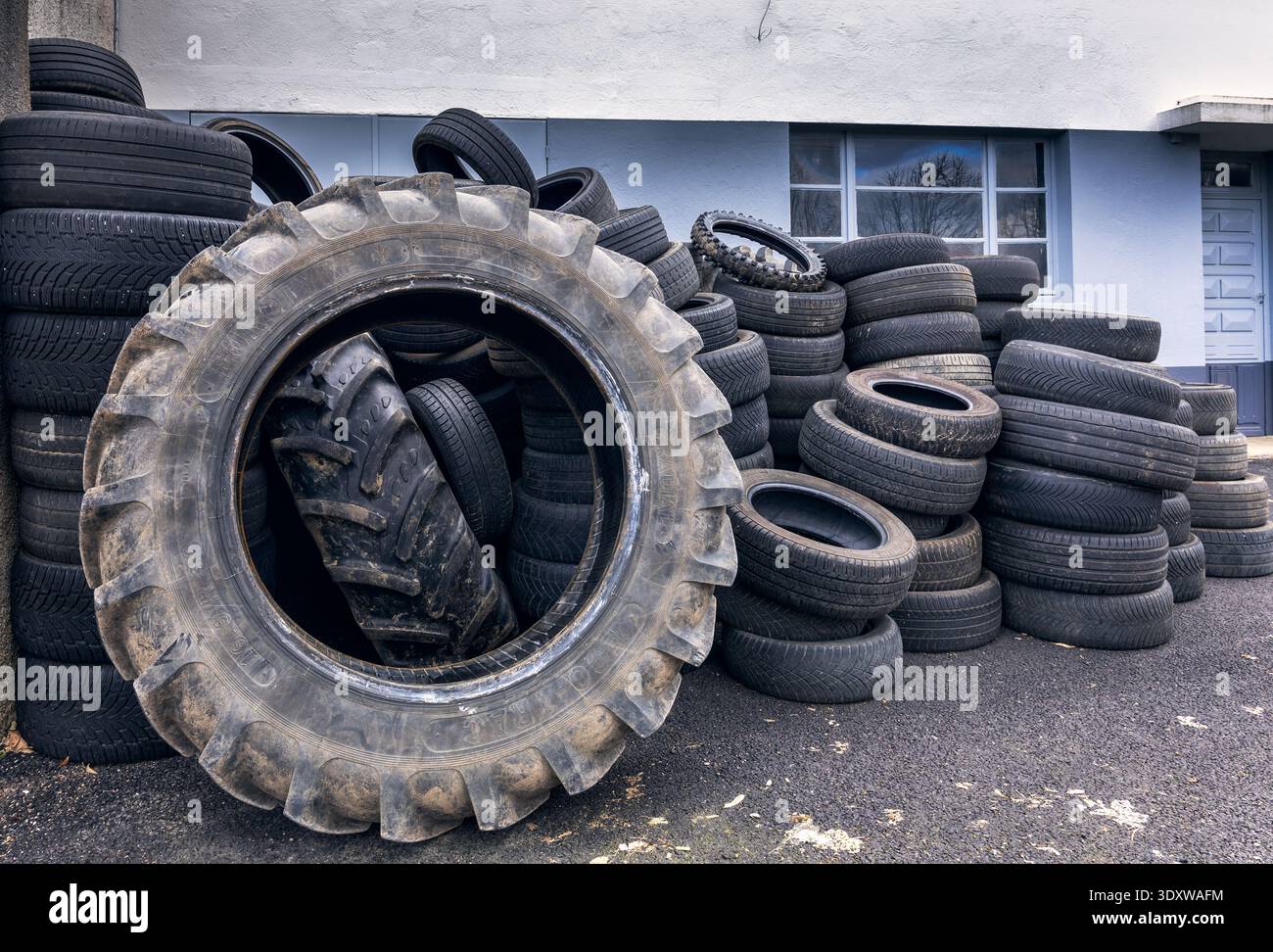 un'enorme pila di pneumatici usati per trattori e veicoli impilati su una parete industriale piana che mostra le superfici in gomma usurate e i rifiuti automobilistici per impieghi gravosi Foto Stock