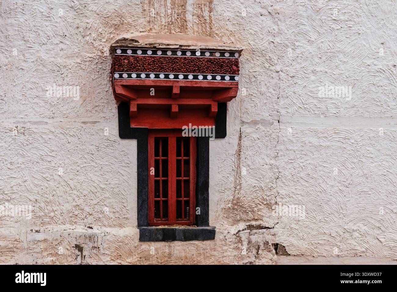 Un'unica finestra tradizionale con un architrave rosso decorativo e finiture nere punteggiate di bianco si trova centrata su una parete dipinta di calce a Hemis Gompa. Foto Stock