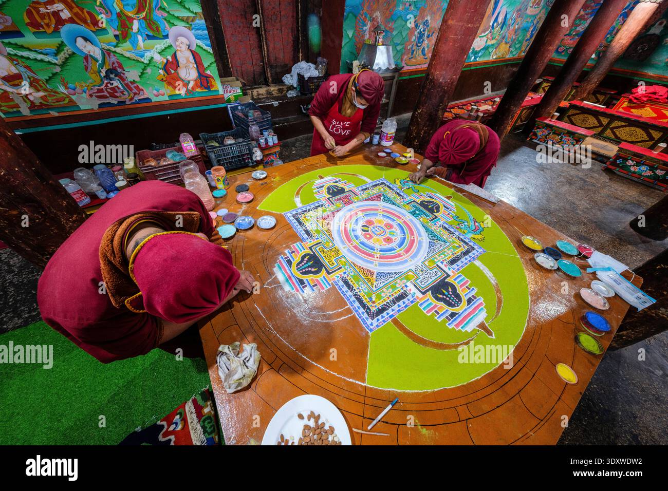 Una vista ad alto angolo mostra diversi monaci che sistemano meticolosamente un grande e colorato mandala di sabbia su una piattaforma rialzata a Hemis Gompa. Foto Stock