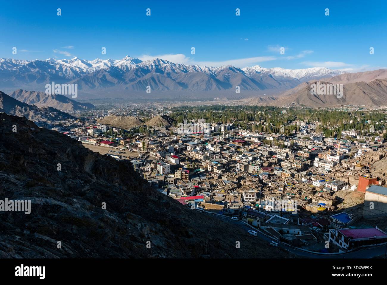 Vista sopraelevata sulla città di montagna di Leh verso la vetta innevata di Stock Kangri che si innalza sopra la catena montuosa di Stok in lontananza. Foto Stock