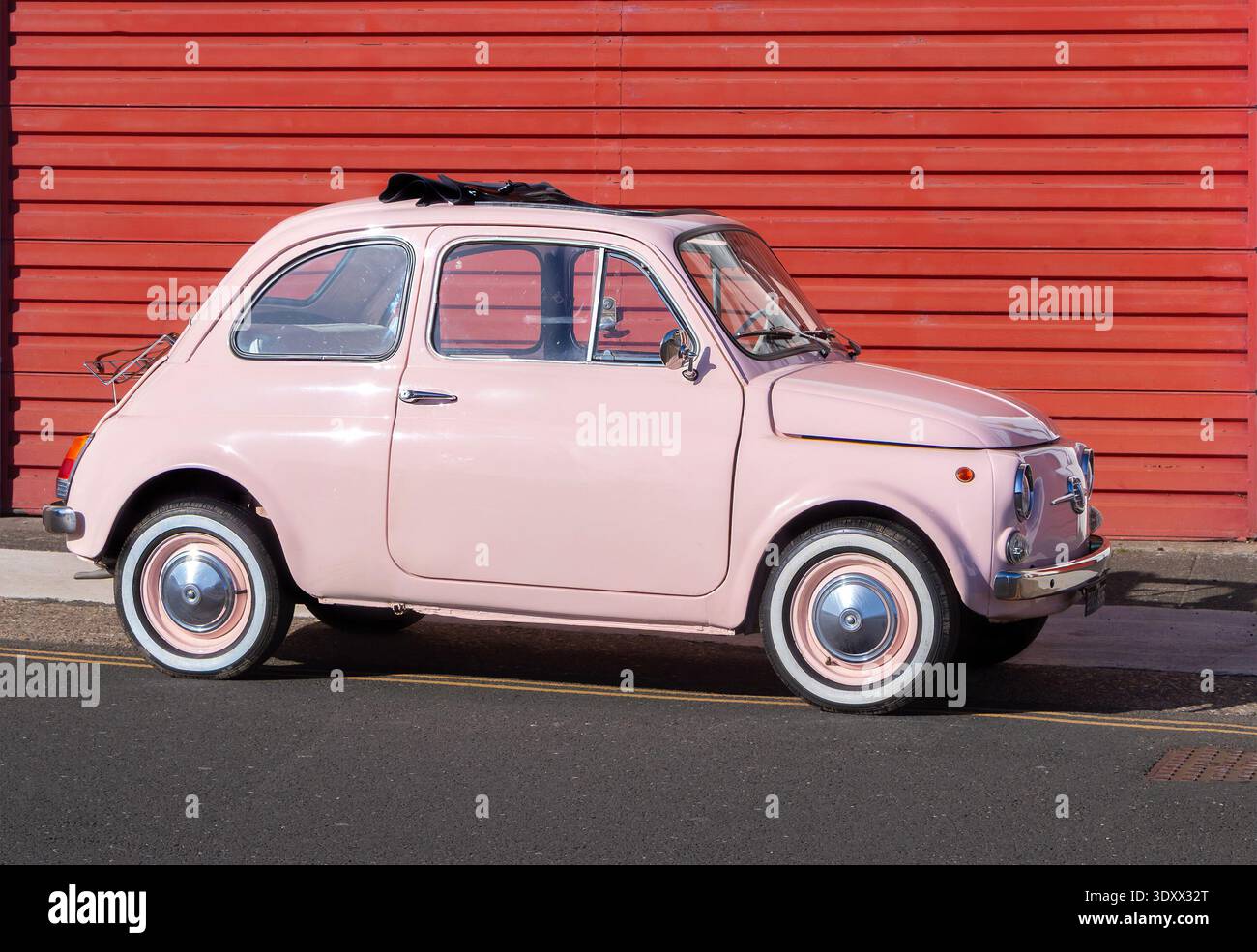 Fiat 500 classica rosa pallido con tetto in tessuto retrattile parcheggiato contro una parete in metallo ondulato rosso vivace - scudi nord, regno unito Foto Stock