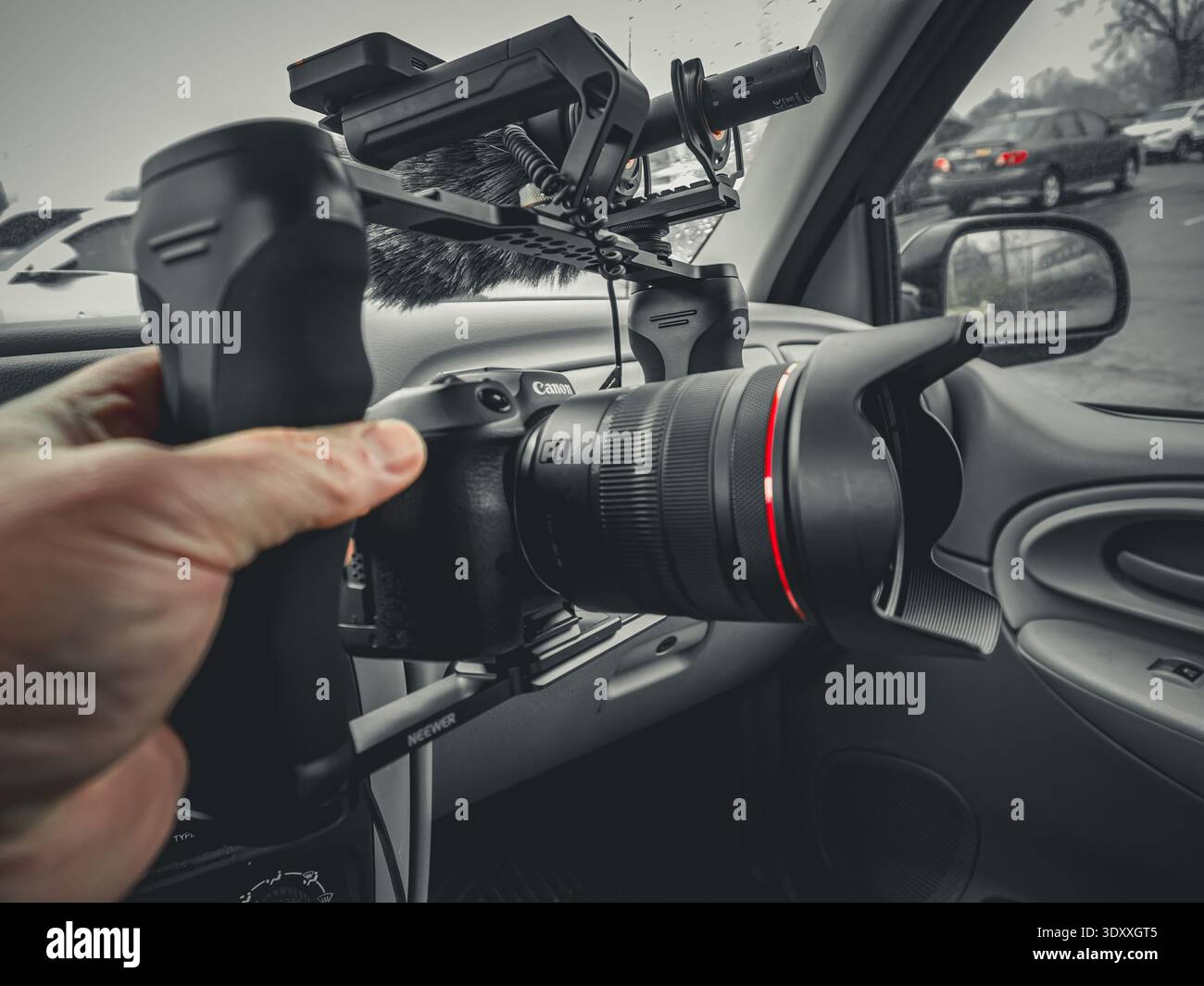 Mano che tiene in mano una macchina fotografica mirrorless Canon con microfono installato all'interno di un'auto, pronta per le riprese o la fotografia Foto Stock
