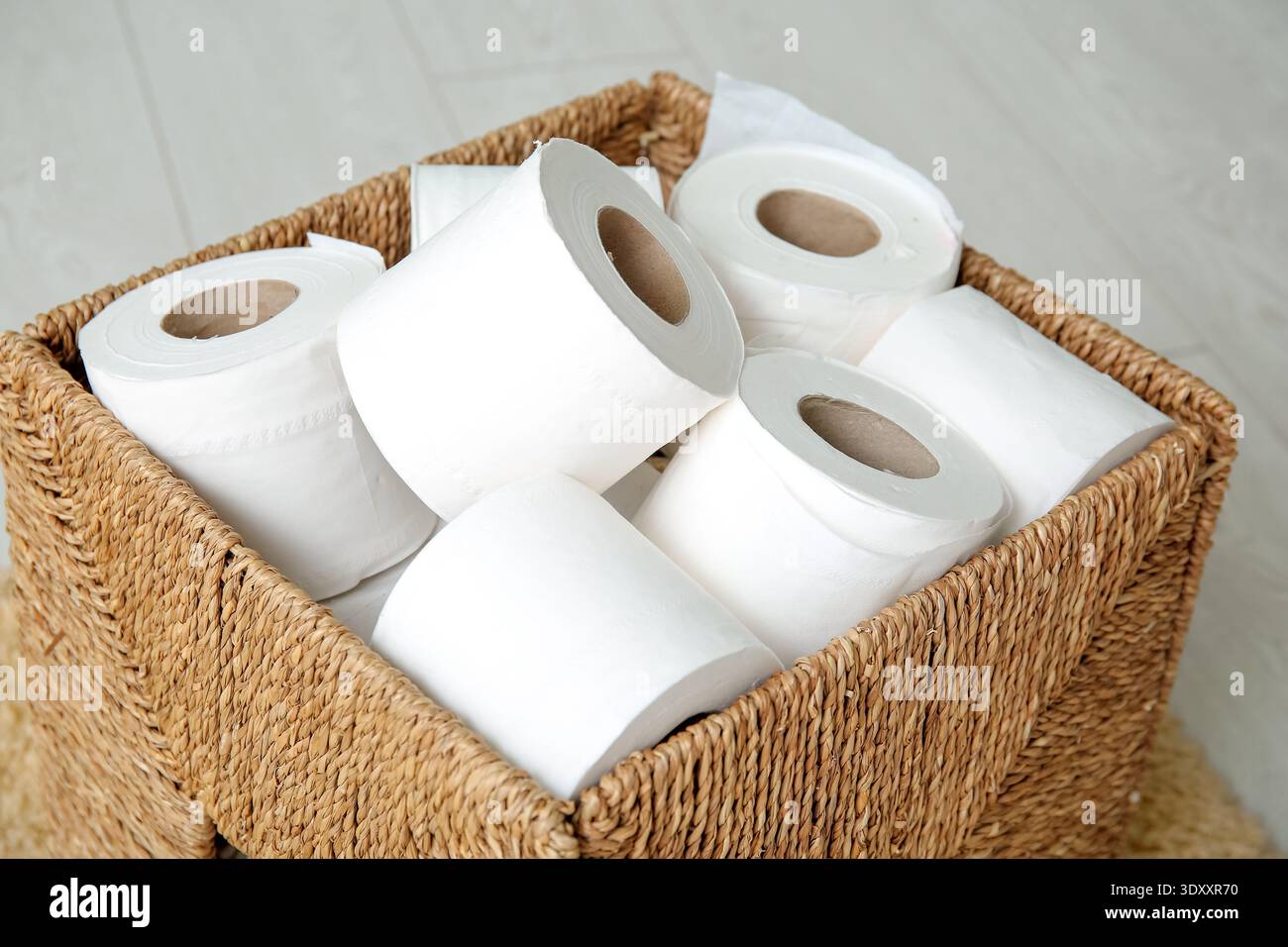 Cestino in vimini con rotoli di carta igienica sul pavimento, primo piano Foto Stock