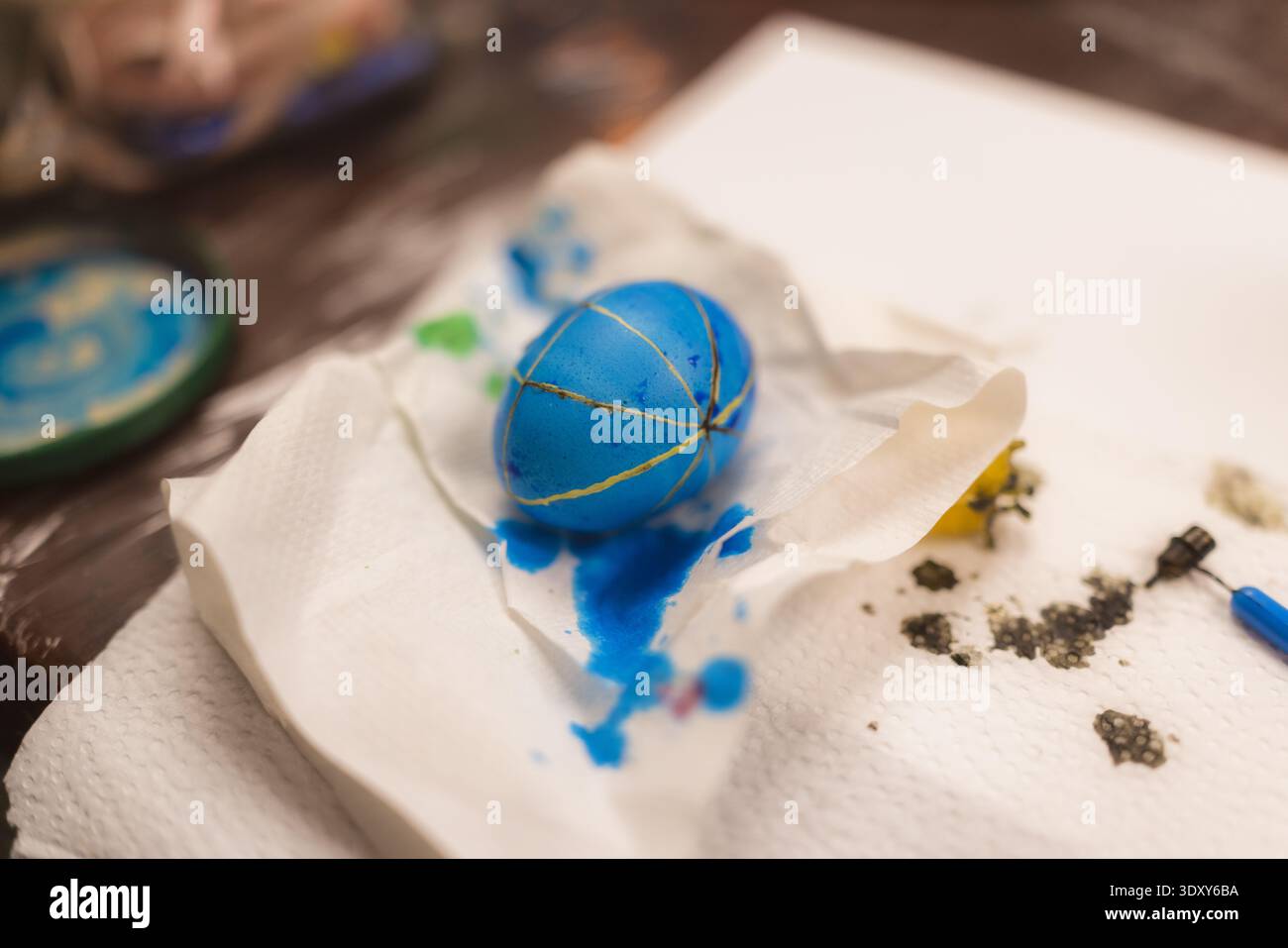 L'uovo blu poggia su un panno di carta stropicciato. Gocce e macchie mostrano un processo creativo. Le impronte digitali e la vernice suggeriscono un'arte pratica. Creare l'atmosfera cattura ar Foto Stock