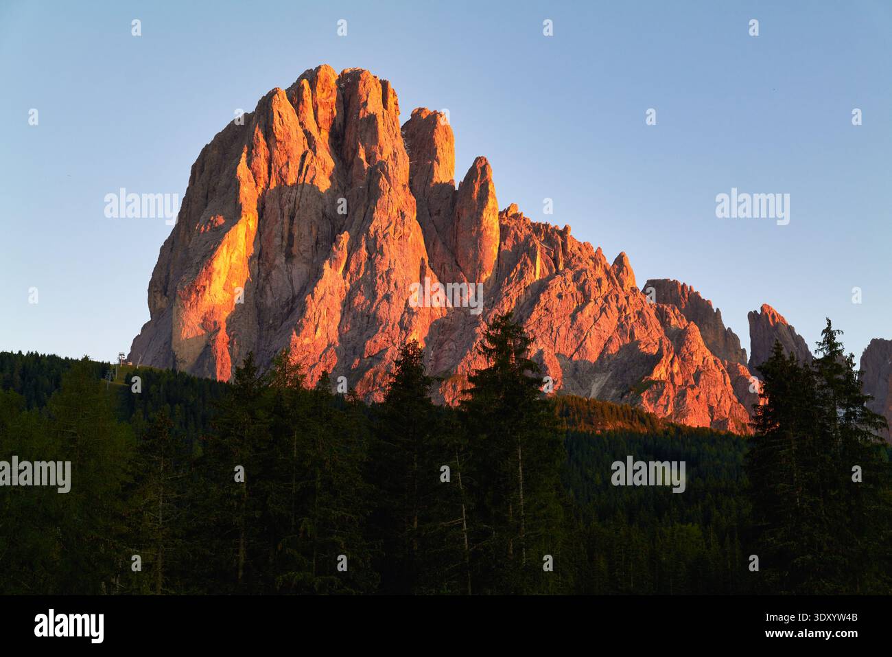 Il Sassolungo si erge alto al tramonto, gettando una luce calda sulle montagne e sugli alberi della Val Gardena, in Italia, creando una vista mozzafiato. Foto Stock