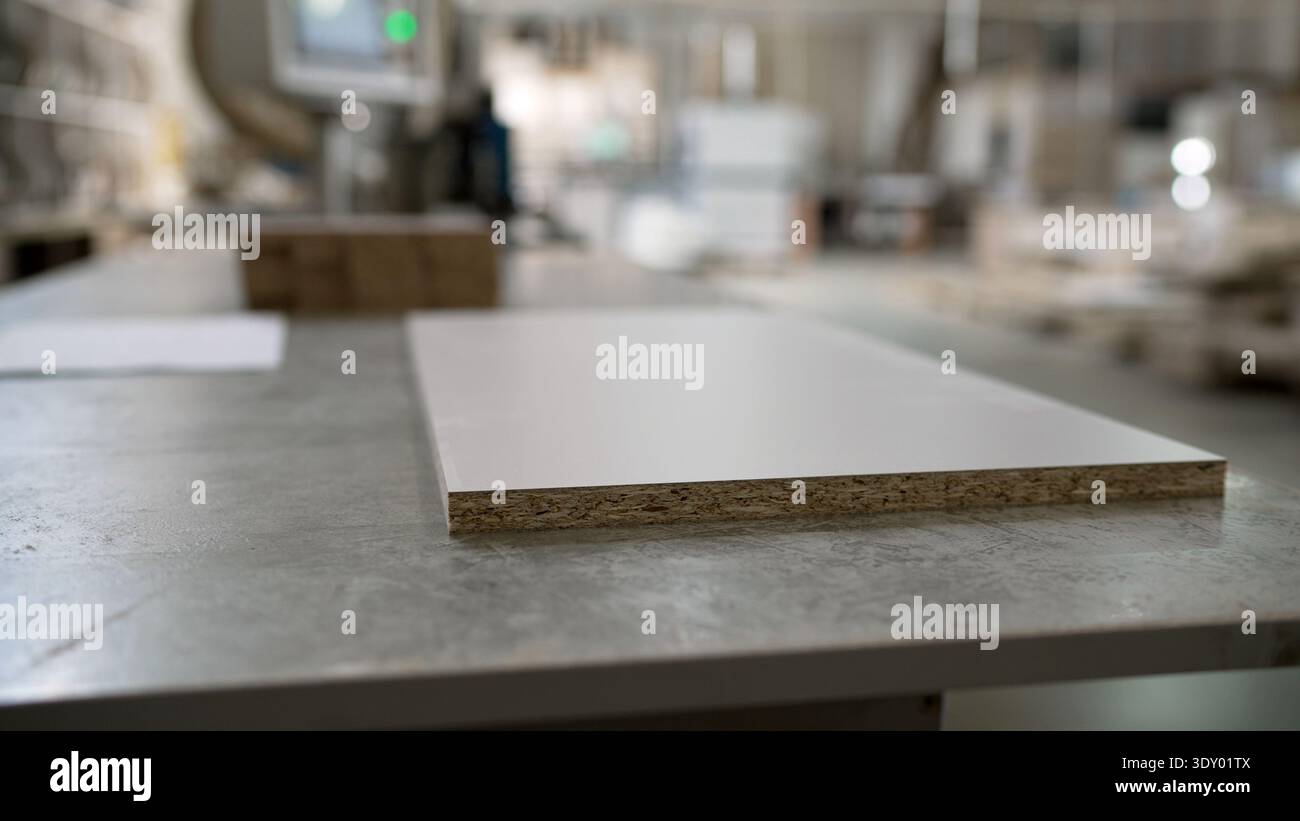 Pannello in truciolato bianco su un tavolo da lavoro in un'officina di produzione di mobili con sfondo sfocato. Foto Stock