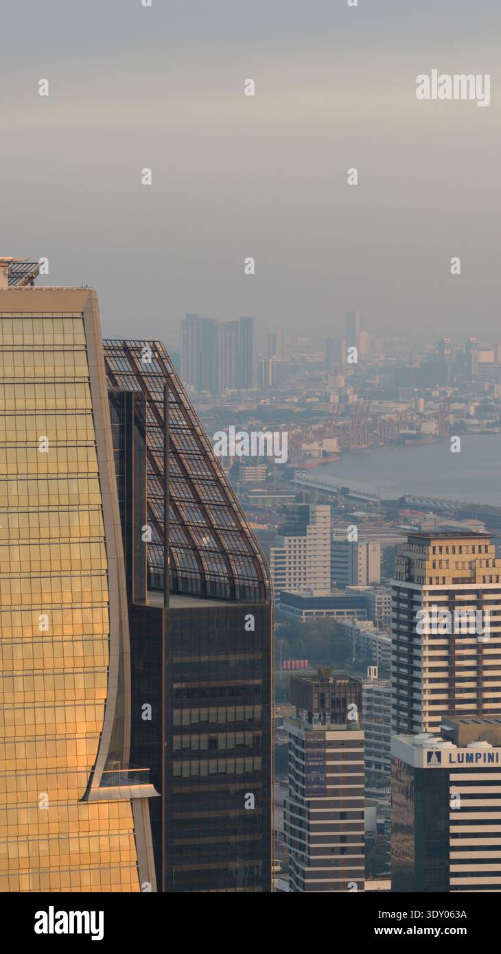 Vista aerea dei grattacieli che piergono attraverso lo skyline nebuloso, riflettendo la luce dorata tra gli arazzi urbani di Bangkok, Bangkok, Thailandia. Foto Stock