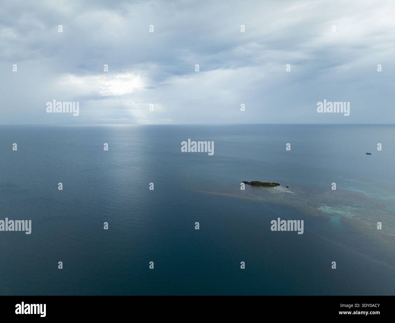 Vista aerea di un isolotto circondato da fondali turchesi nel profondo blu del mare sotto un cielo striato di luce solare, Karimunjawa, Giava centrale, Indon Foto Stock