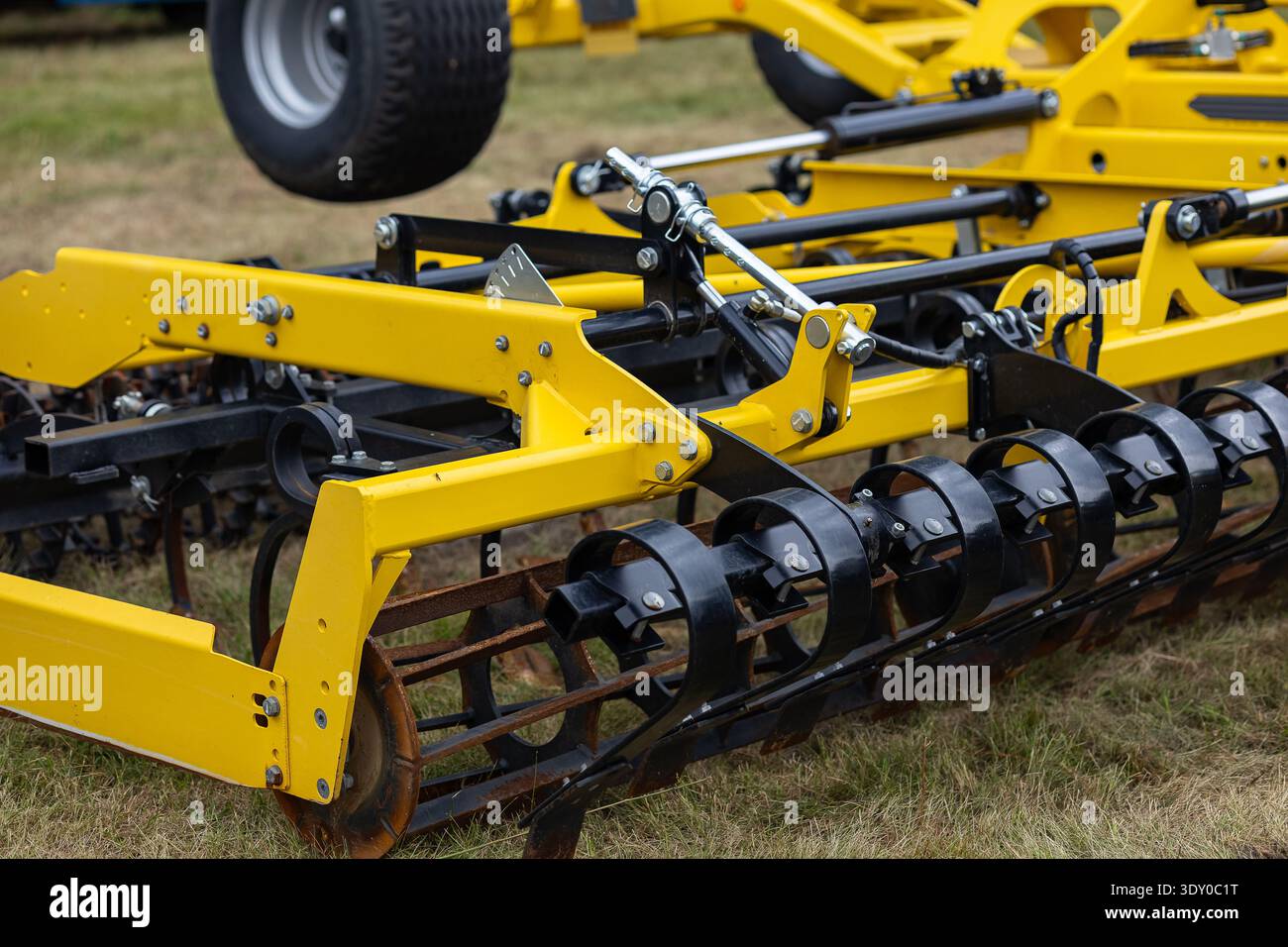 Primo piano dell'impianto idraulico su un sottoradiatore agricolo giallo con cilindri, tubi flessibili e rulli metallici neri. Macchinari agricoli moderni Foto Stock
