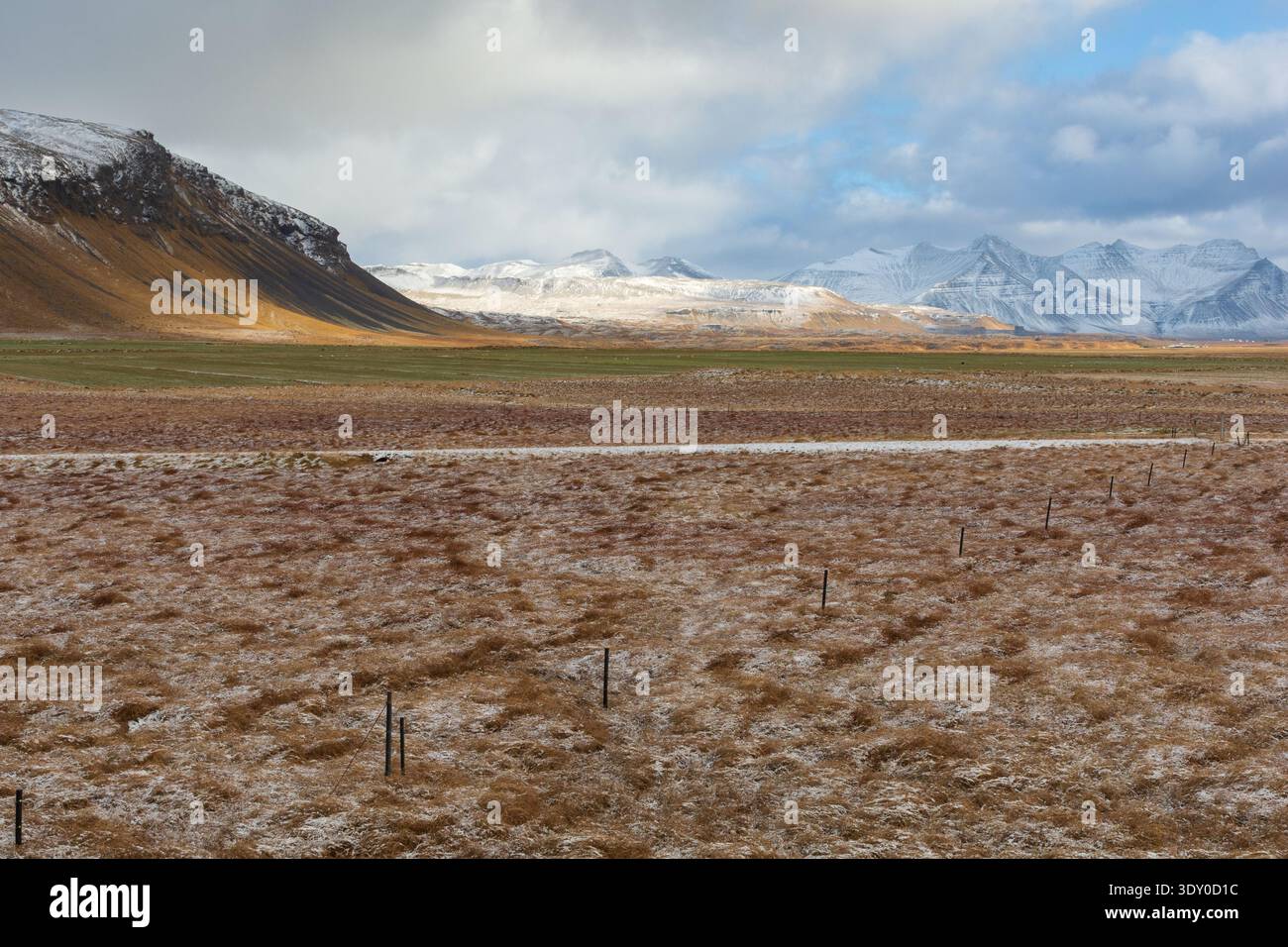 Vista dei campi dorati che incontrano le montagne innevate sotto un cielo di blu e grigi morbidi, creando un tranquillo paesaggio islandese, la penisola di Snæfellsnes Foto Stock