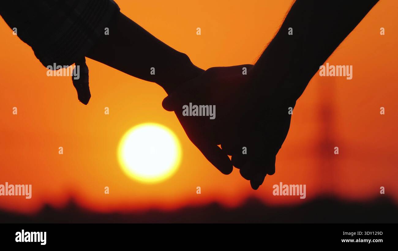 Giovane coppia che tiene le mani sullo sfondo di un grande sole che tramonta Foto Stock