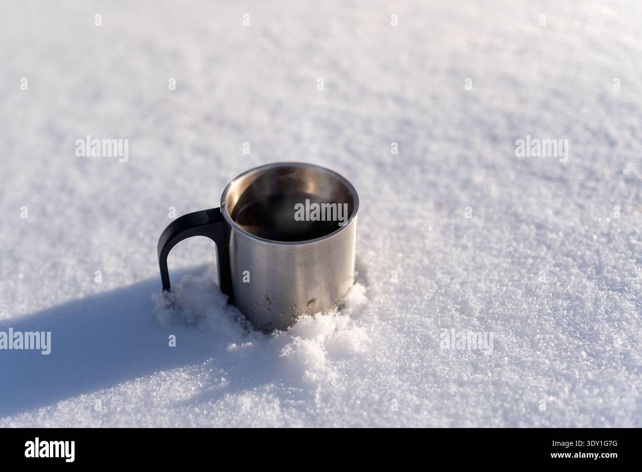 Tazza da campeggio in acciaio inox in piedi nella neve fresca nelle soleggiate giornate invernali. Bevanda calda all'aperto e avventura invernale con spazio fotocopie. Foto Stock