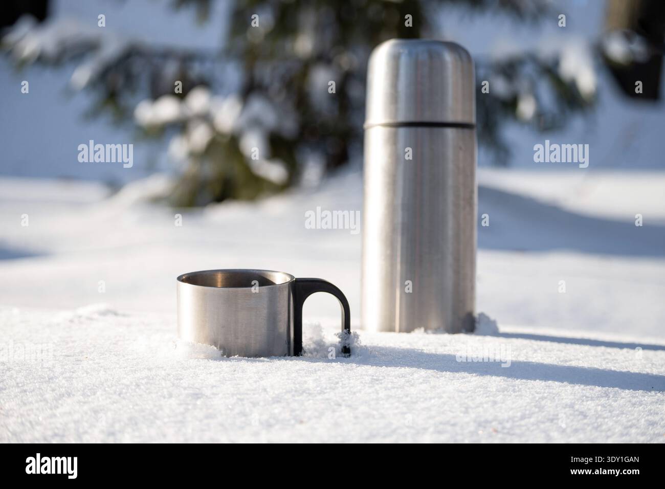 Vaso termos in metallo e tazza in acciaio in posizione di neve fresca durante le soleggiate giornate invernali. Bevanda calda all'aperto. Picnic invernale con bevande calde. Foto Stock