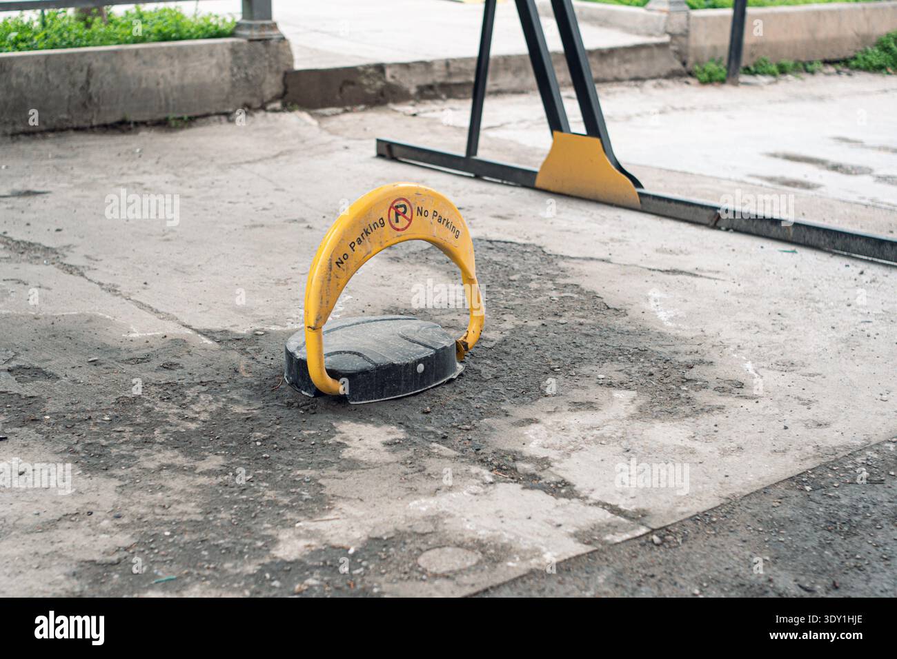 Un bagagliaio giallo con il cartello "No Parking" è fissato su una superficie asfaltata sporca in un'area di parcheggio. Foto Stock