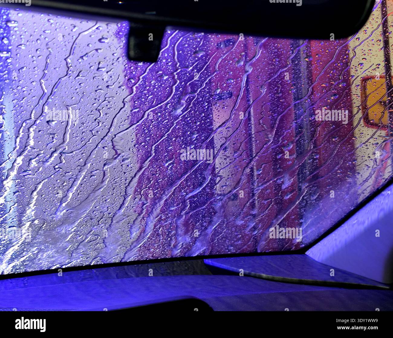 L'autolavaggio automatico applica una cera protettiva alla fine del lavaggio. Dall'interno dell'abitacolo, una vista dal finestrino del gocciolamento di cera. Foto Stock