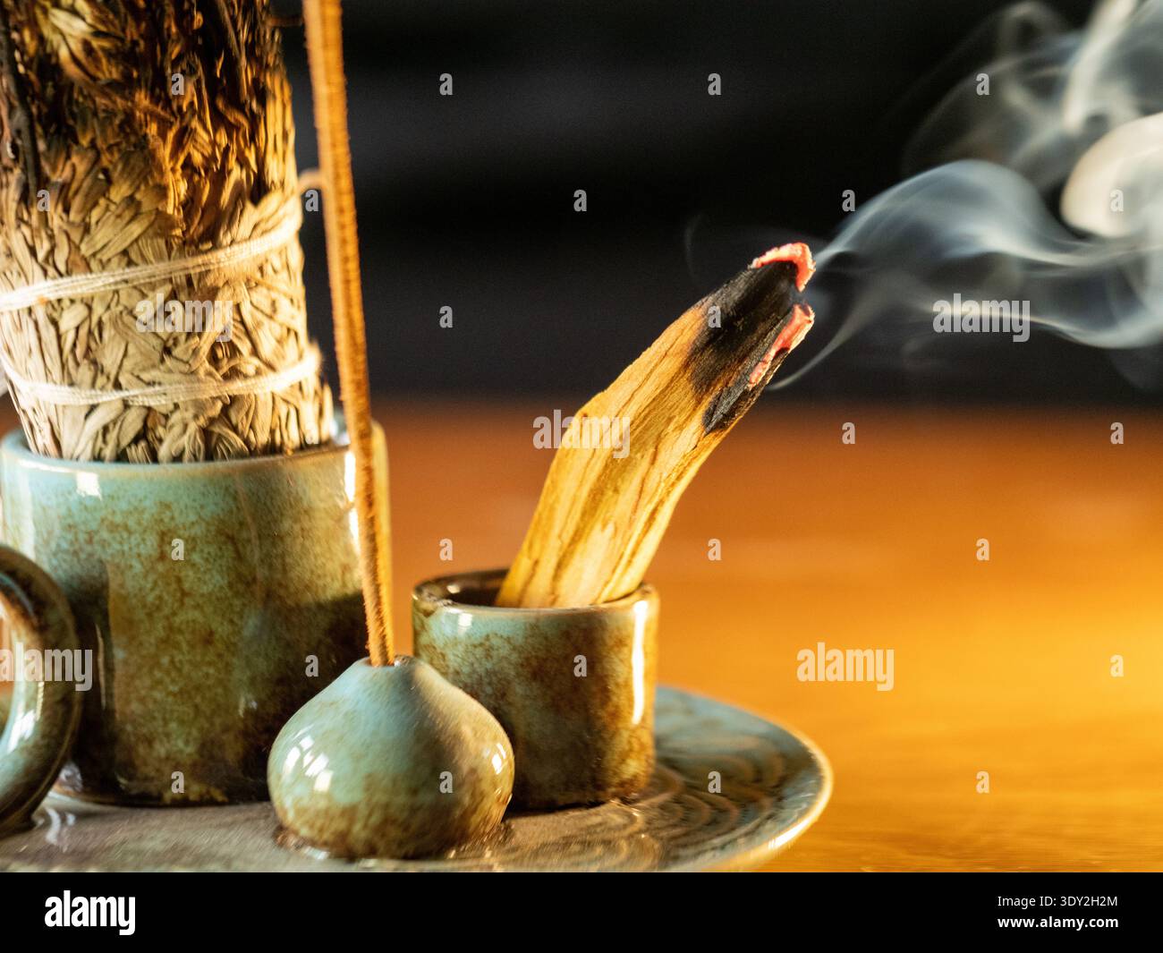 Il fumo si arriccia delicatamente con un bastoncino di salvia bruciato. Il supporto in ceramica consente di alloggiare il gruppo di saldatura. La luce calda inonda la scena di un bagliore dorato. Stillness sugg Foto Stock