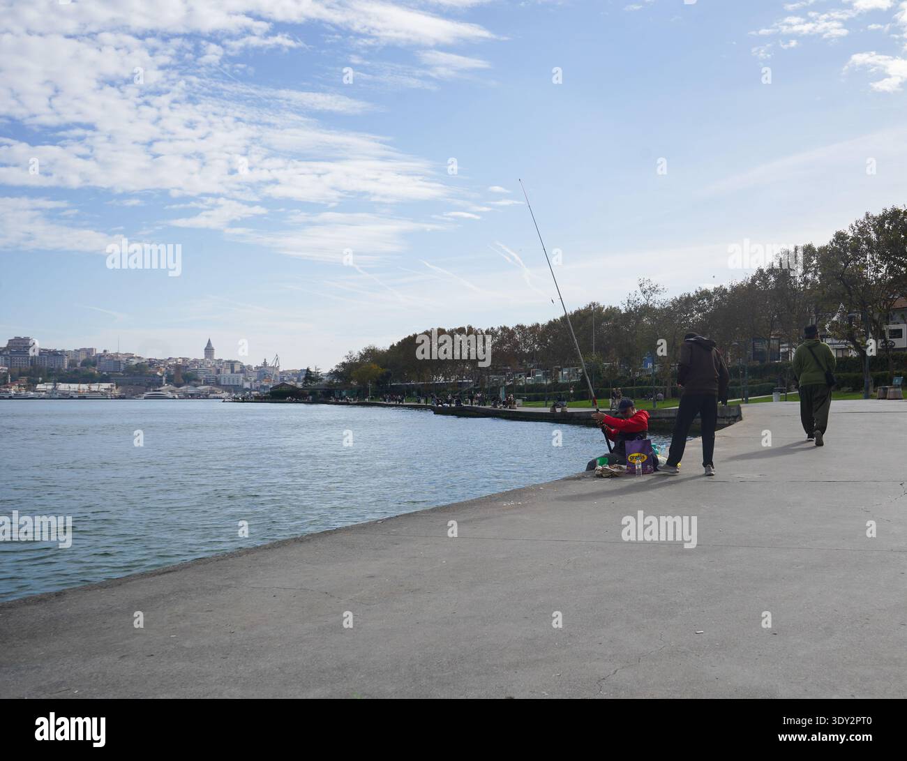 Pescatori sul lungomare del Corno d'Oro, con la Torre Galata e lo skyline distanti sotto un cielo azzurro. Foto Stock