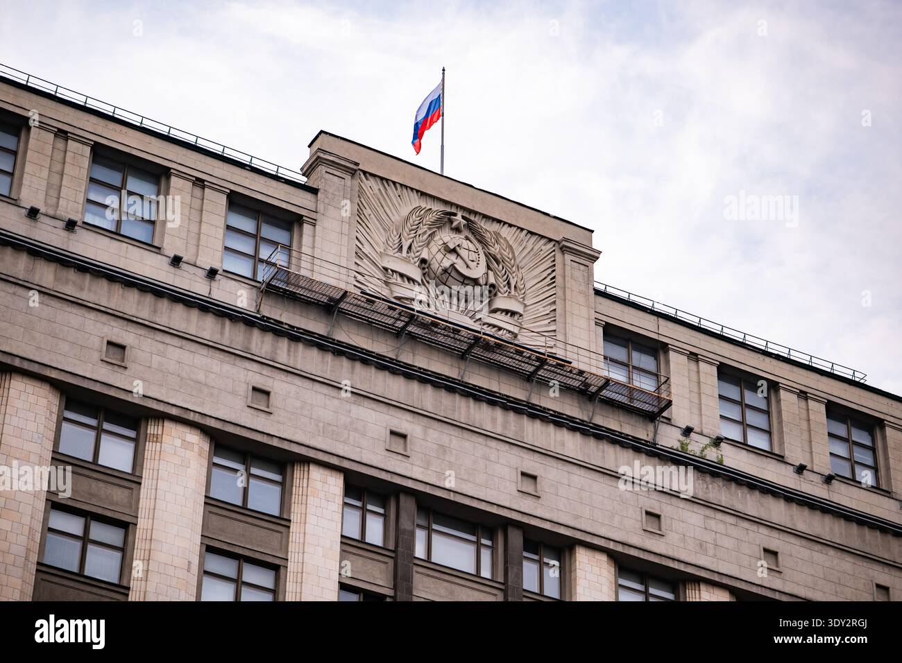 Bandiera russa che sventola sopra l'edificio della Duma di Stato con stemma sovietico in rilievo, Mosca Foto Stock