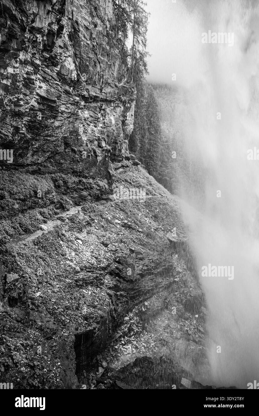 Le cascate di Johannes scendono elegantemente dalle scogliere rocciose di Obertauern, Austria. Circondata da alberi alpini, la cascata crea un'atmosfera nebbiosa, perfetta per gli amanti della natura e degli escursionisti. Foto Stock