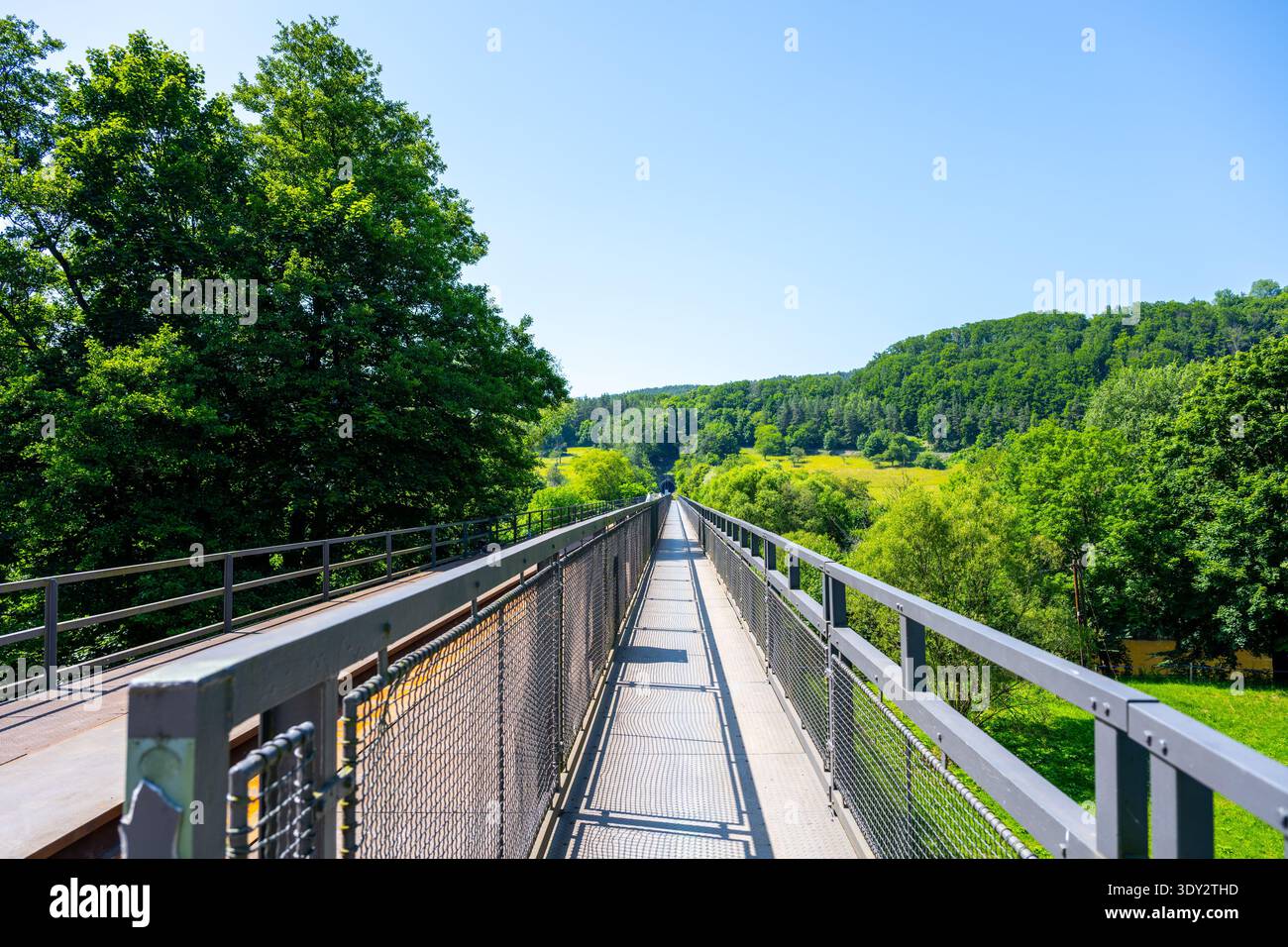 Un ponte ciclabile Greenway Jizera attraversa il fiume. Collega sentieri per andare in bicicletta e camminare attraverso alberi verdi e colline sullo sfondo in una giornata limpida. Foto Stock