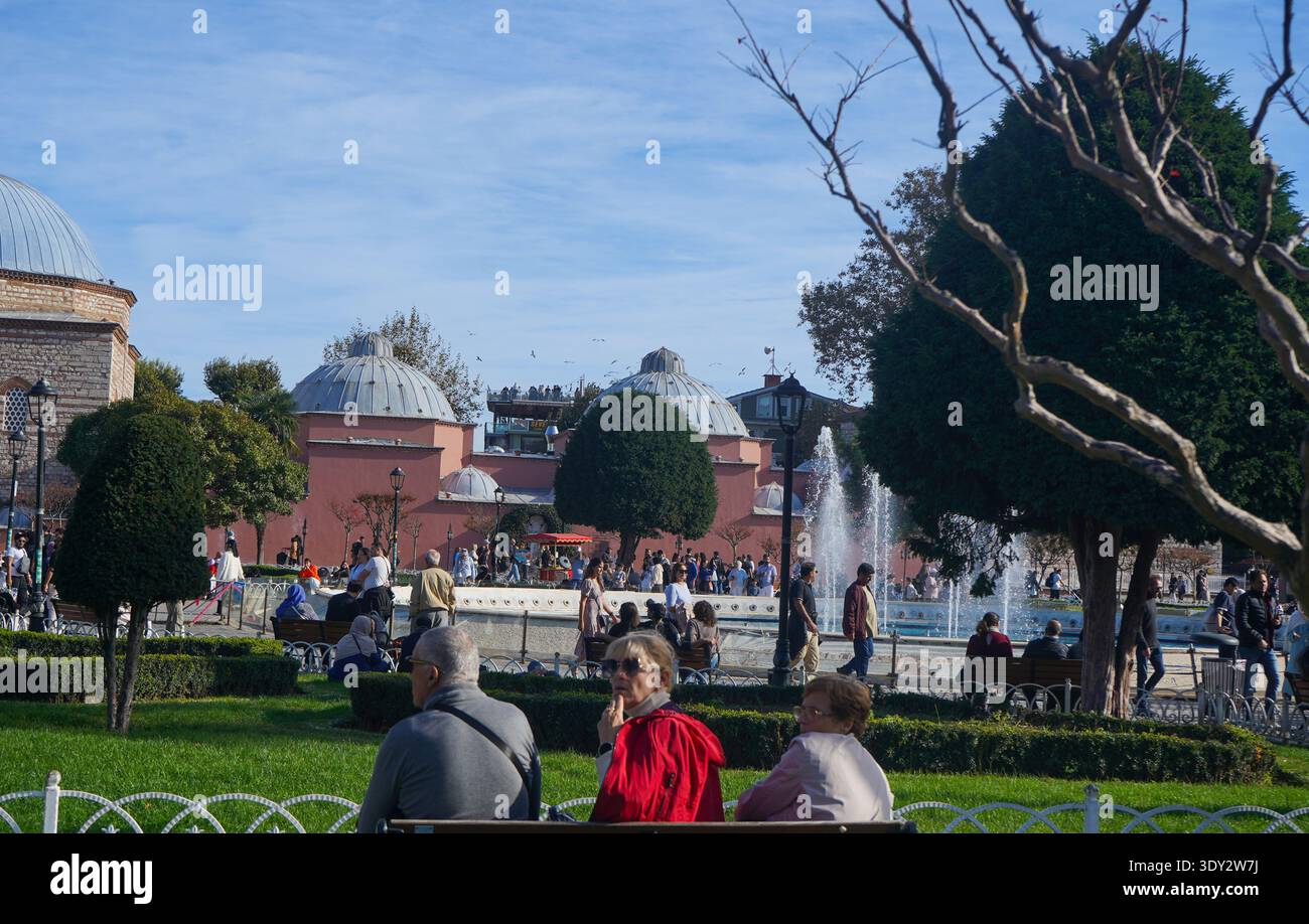Parco pubblico di Istanbul con persone che si rilassano sulle panchine vicino a una grande fontana. Cupole in piombo in stile ottomano tradizionale e architettura storica in pietra. Foto Stock
