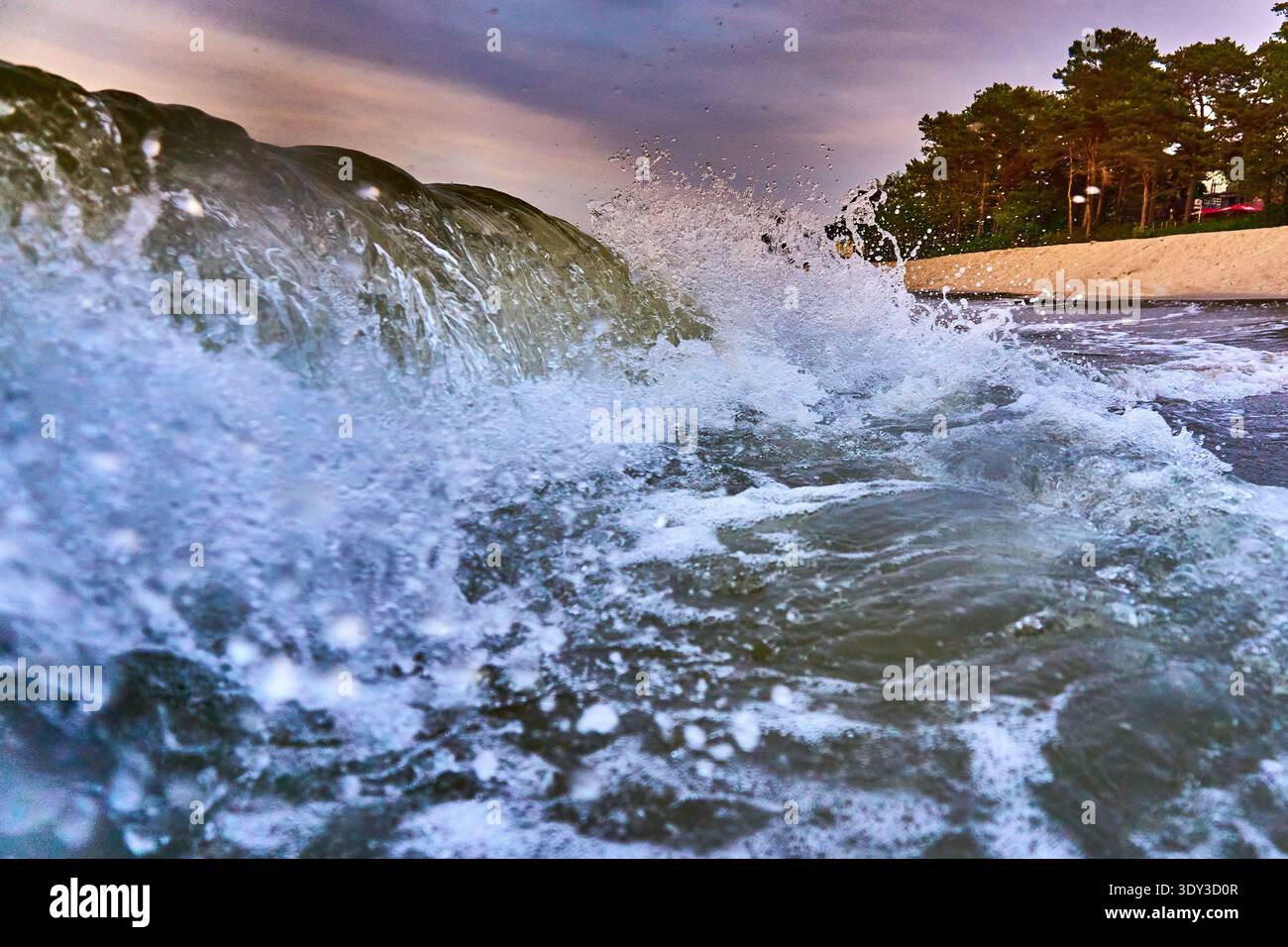 Uno scatto dinamico e ravvicinato di grandi onde che si infrangono e spruzzano, catturato da un'angolazione ridotta. L'acqua è piena di schiuma e movimento, con goccioline che volano Foto Stock