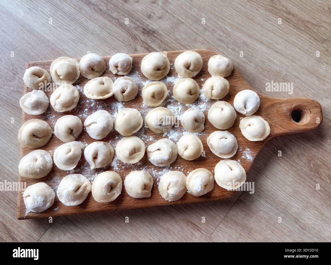 Gnocchi crudi fatti in casa su tagliere di legno con farina. Processo di cottura tradizionale, vista dall'alto, luce naturale, cucina rustica. Foto Stock
