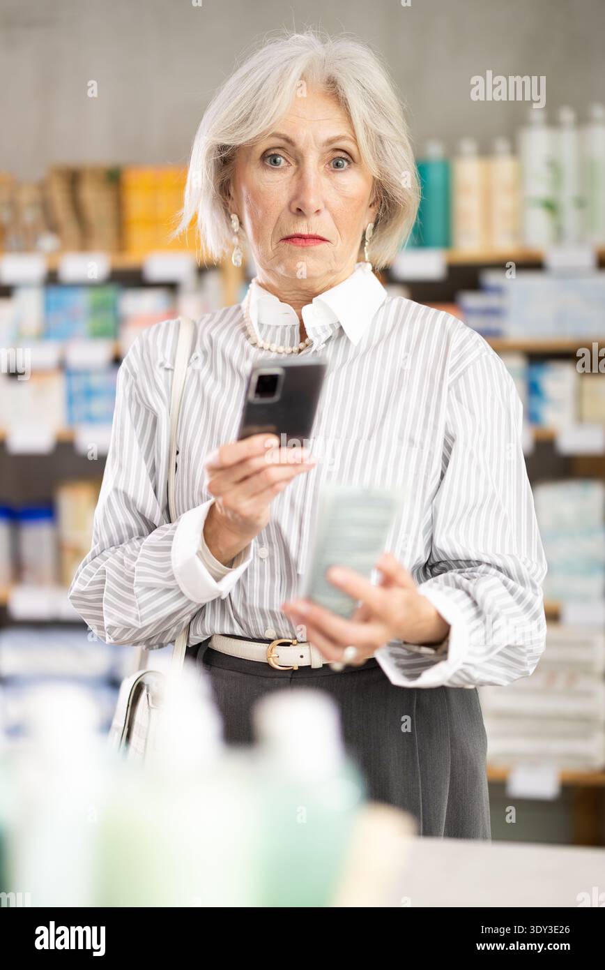 Donna matura in abiti estivi scansiona il codice sulla confezione della crema per controllare la data di scadenza Foto Stock