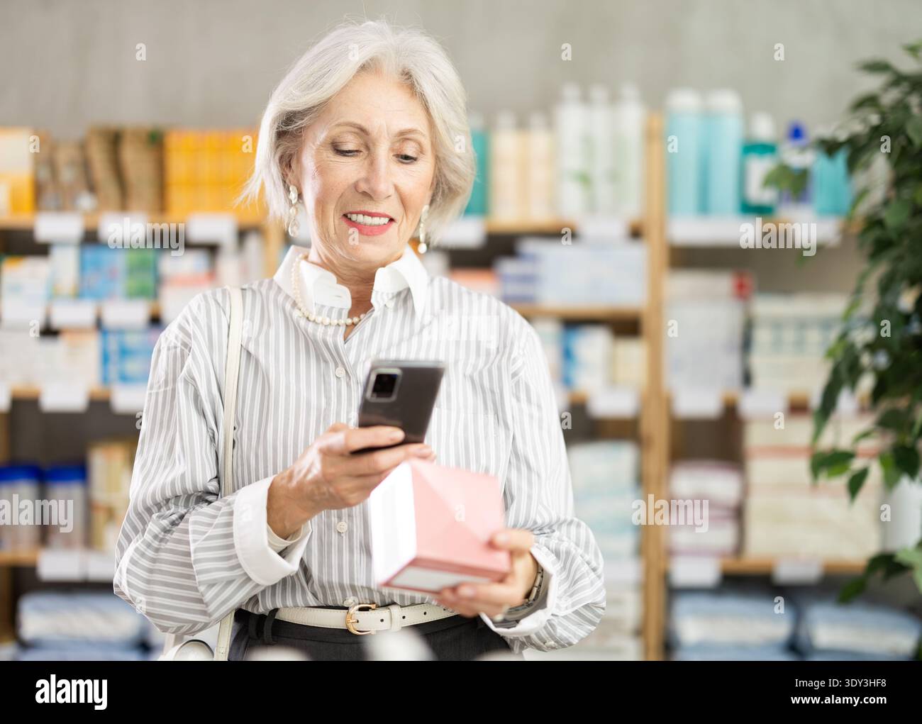 Donna anziana in abiti estivi scansiona il codice sulla confezione di pillole per controllare la data di scadenza Foto Stock