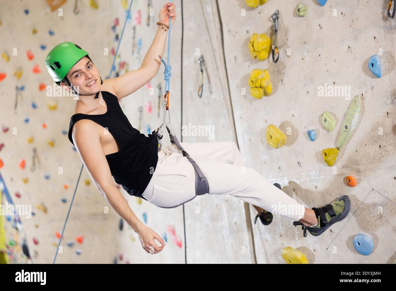 l'uomo con casco di sicurezza e con la fune di sicurezza si appende vicino alla parete di arrampicata in palestra Foto Stock