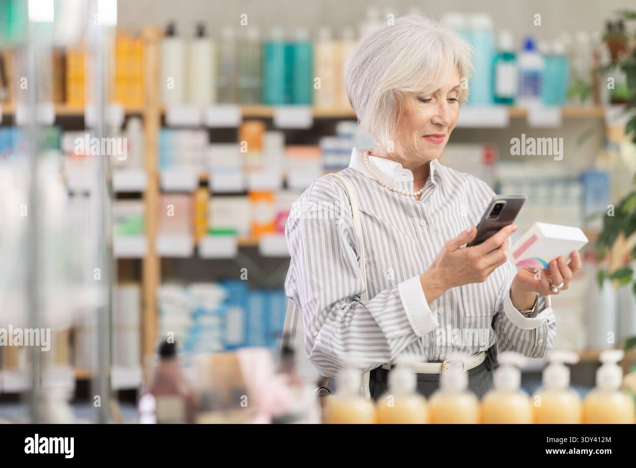 Donna anziana in abiti estivi scansiona il codice sulla confezione di pillole per controllare la data di scadenza Foto Stock