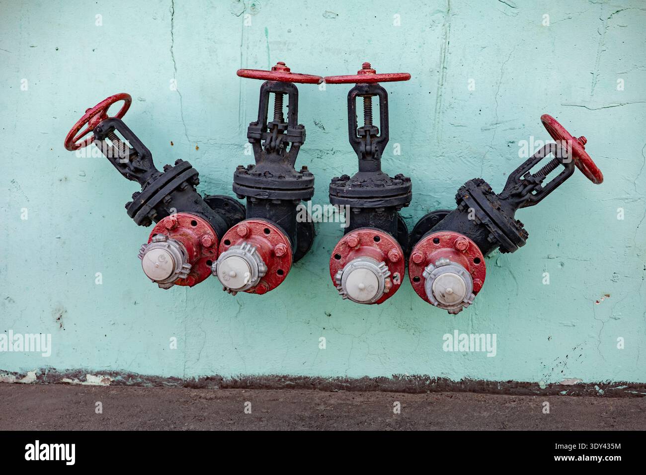 Valvole dell'acqua industriali con ruote rosse su una parete verde chiaro, per garantire la sicurezza antincendio Foto Stock