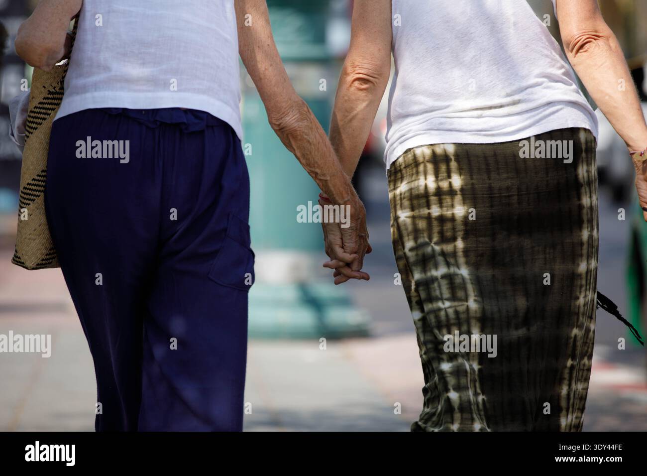 Donne anziane che tengono le mani camminano insieme, pedonale che cammina alla luce del sole, pelle delle mani, vista posteriore, a Tha Chang. Foto Stock