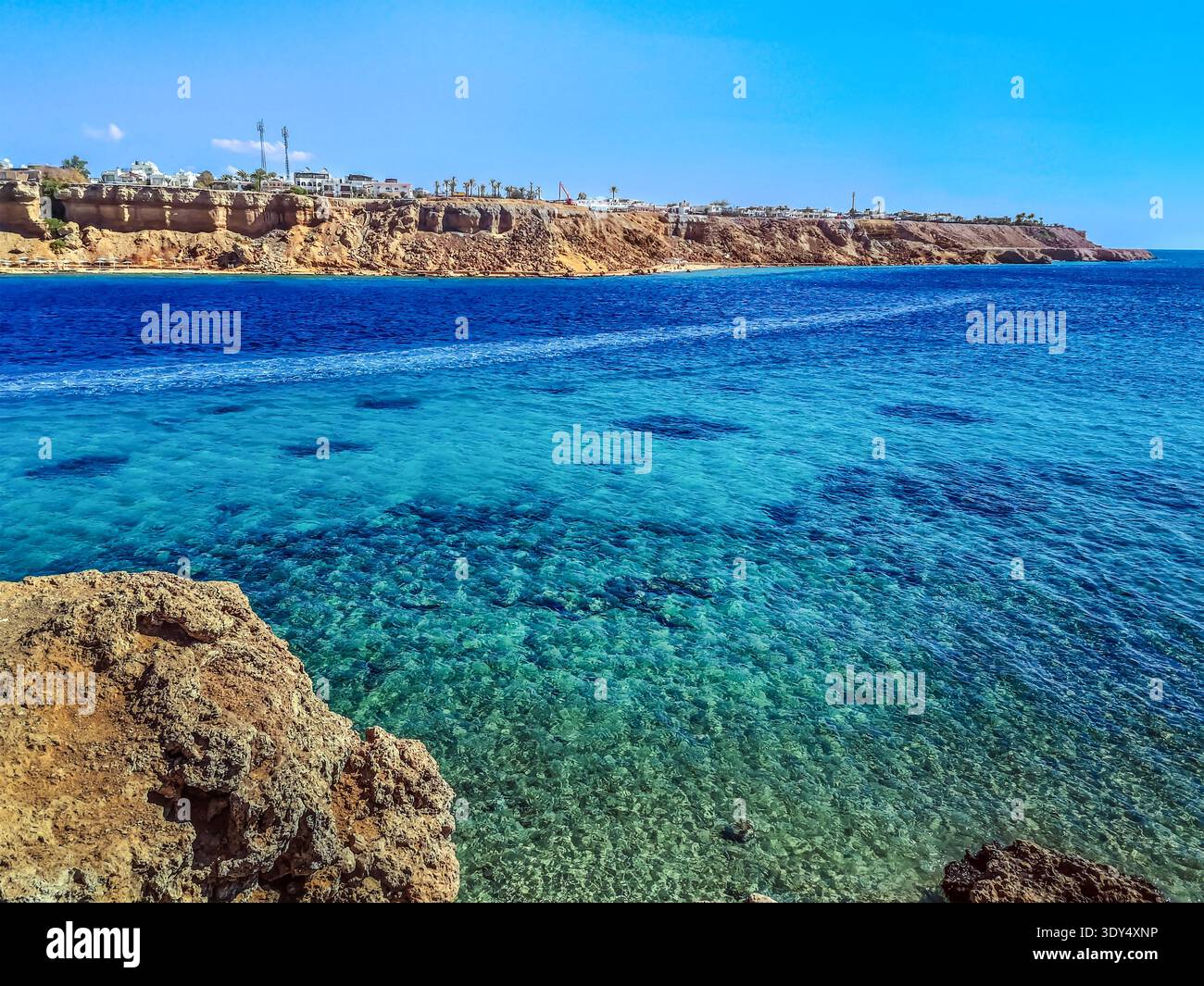Vista dall'alto dalla scogliera al Mar Rosso nella baia di Sharm el-Maya a Sharm El Sheikh, Egitto. Incredibile paesaggio marino con acqua azzurra contro il paesaggio urbano del deserto Foto Stock