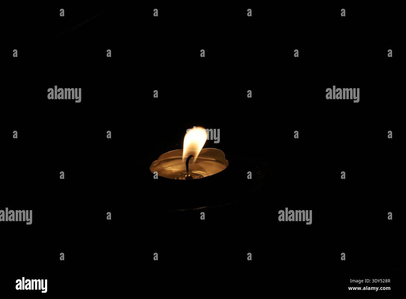 Primo piano minimalista di una singola fiamma di candela che si illumina su uno sfondo scuro, trasmettendo spiritualità, meditazione e riflessi tranquilli. Foto Stock