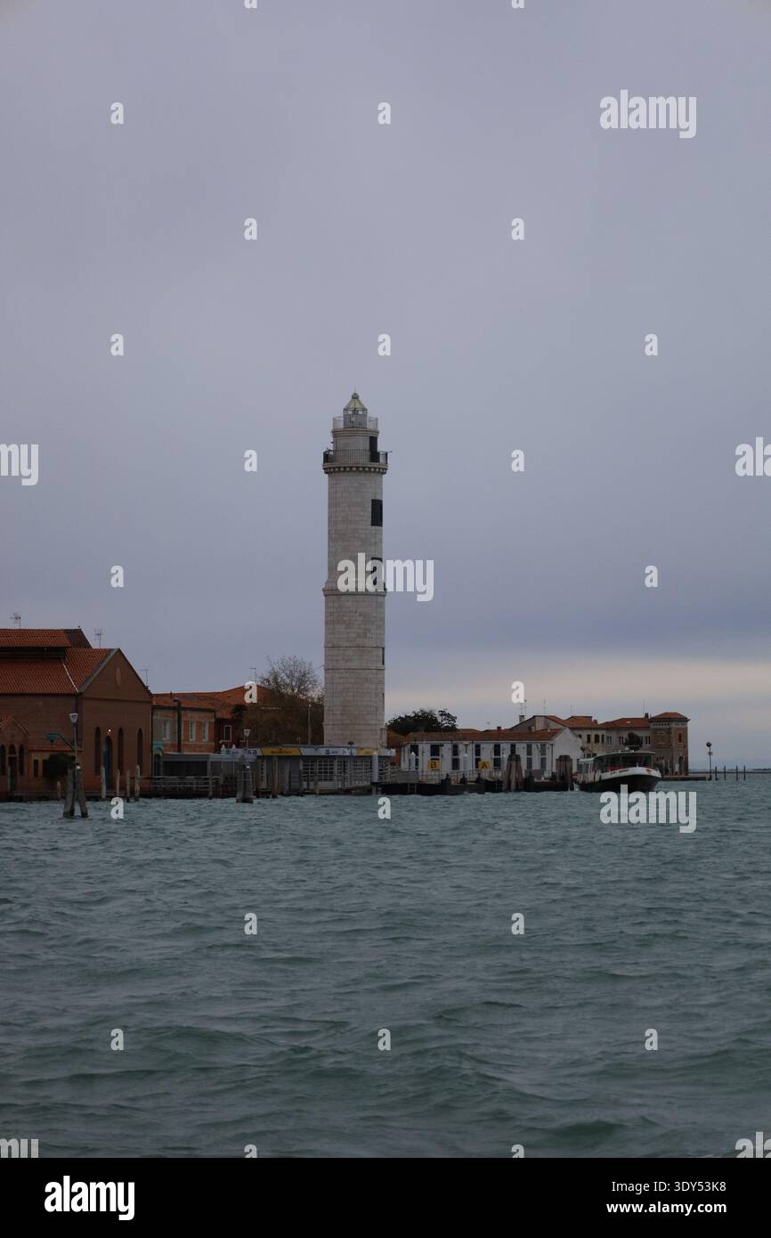 Faro che si erge lungo il lungomare della laguna di Venezia sotto una drammatica coltre di nuvole. Foto Stock