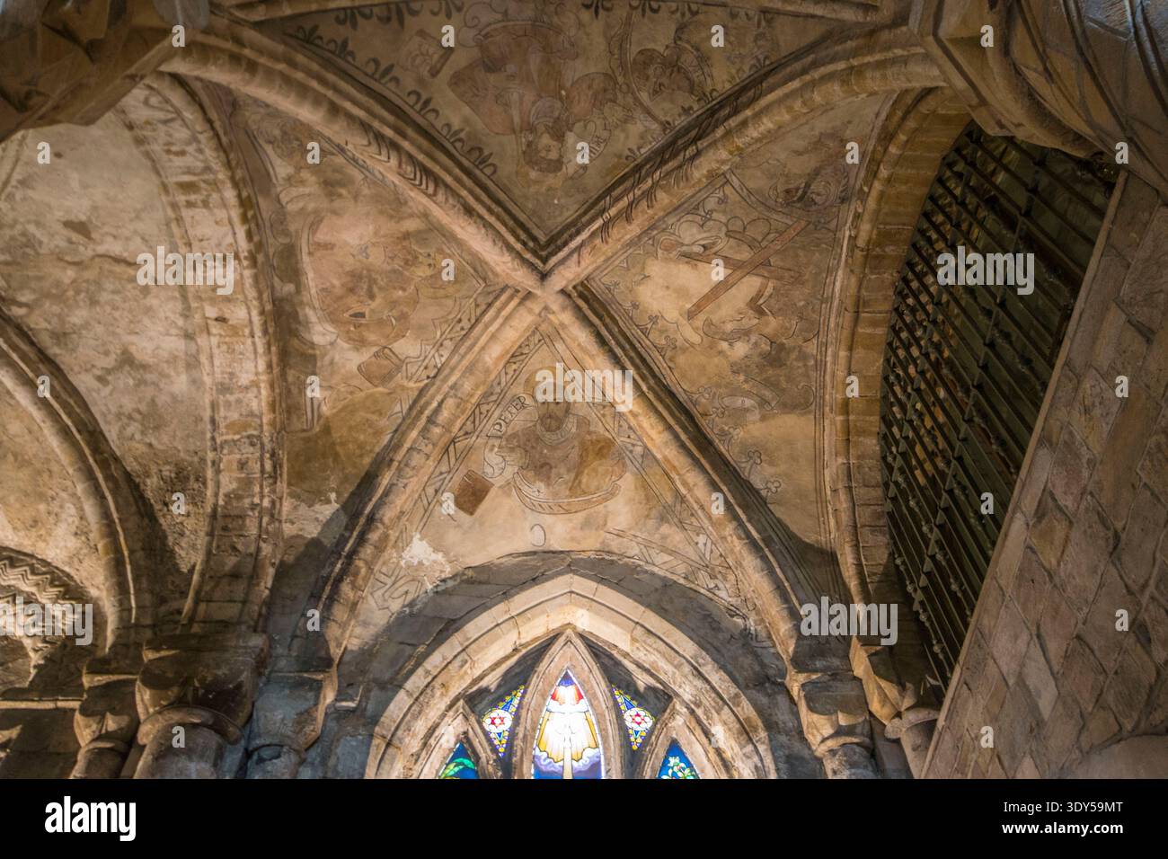 Affreschi medievali intricati adornano la muratura in pietra di un soffitto a volta quadripartita ad arco all'interno di un'antica chiesa storica. Foto Stock