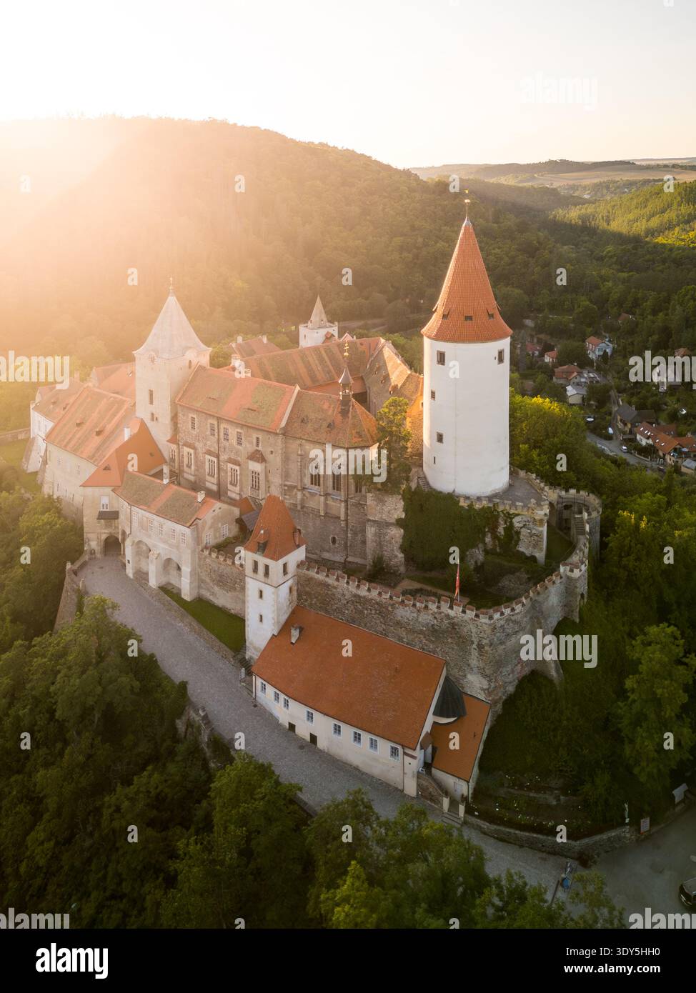 Il Castello di Krivoklat, situato nella Boemia centrale, mostra il suo fascino medievale mentre il sole tramonta dietro le colline, gettando un caldo bagliore sull'antica struttura e sul paesaggio circostante. Foto Stock