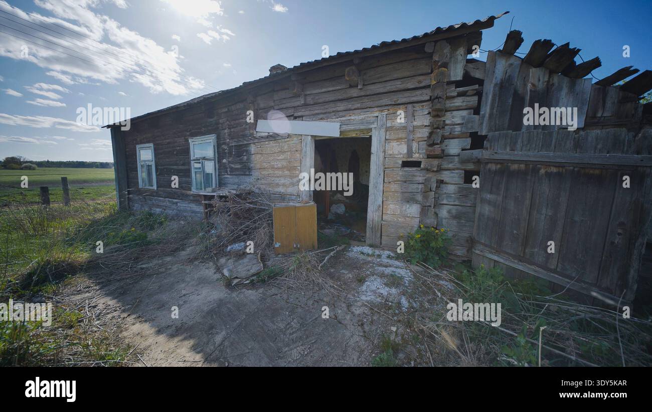 Casa rurale abbandonata in legno che mostra degrado e abbandono in un vasto paesaggio verde Foto Stock