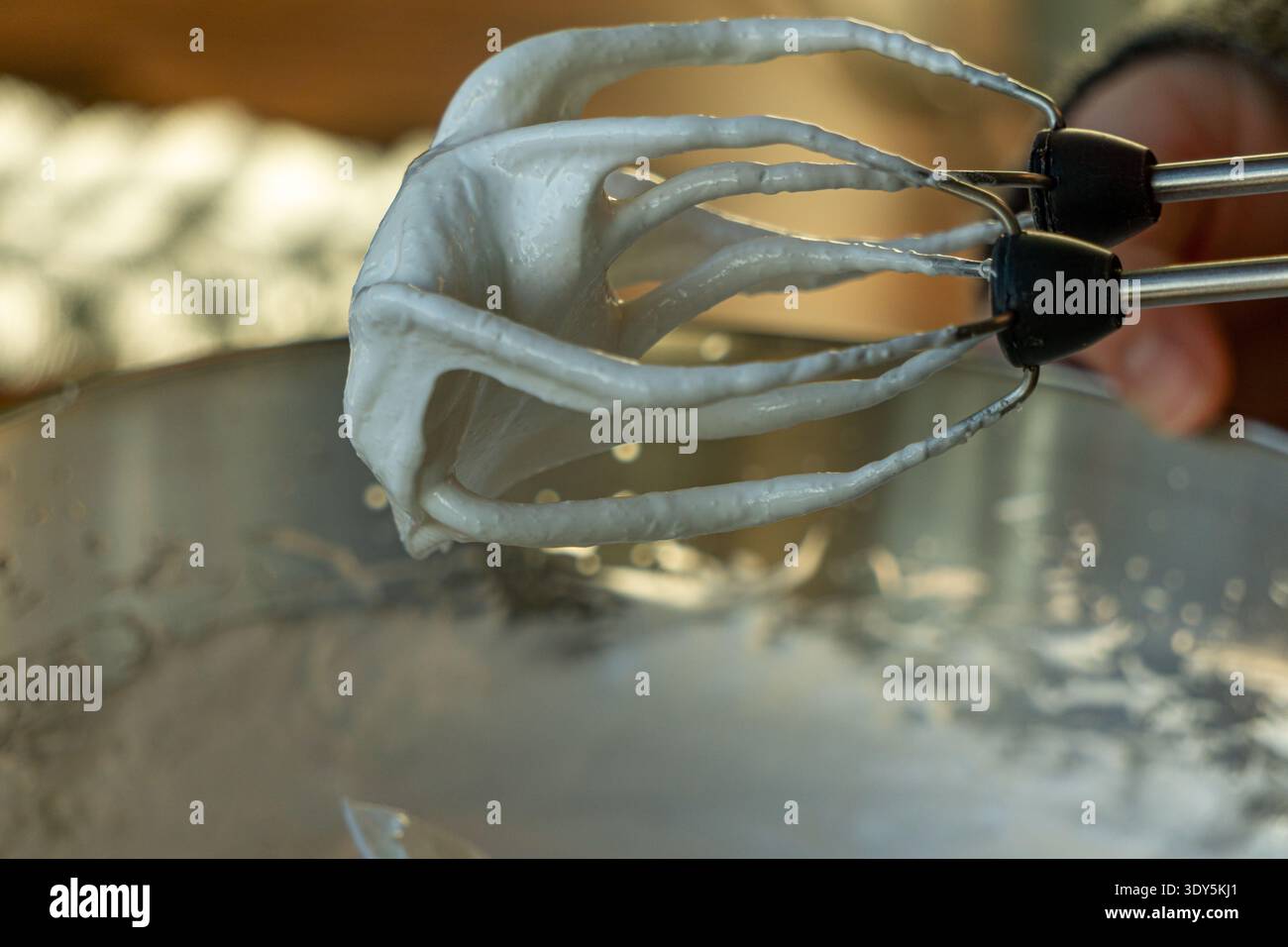 Primo piano di meringa lucida spessa che reggono picchi rigidi sulle frullatrici sopra un recipiente in acciaio inossidabile. Foto Stock