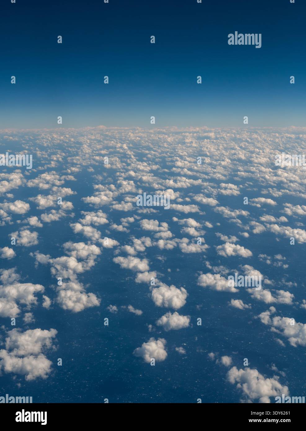 Guardando verso il basso su soffici nuvole nel cielo blu dalla finestra dell'aereo. Foto Stock