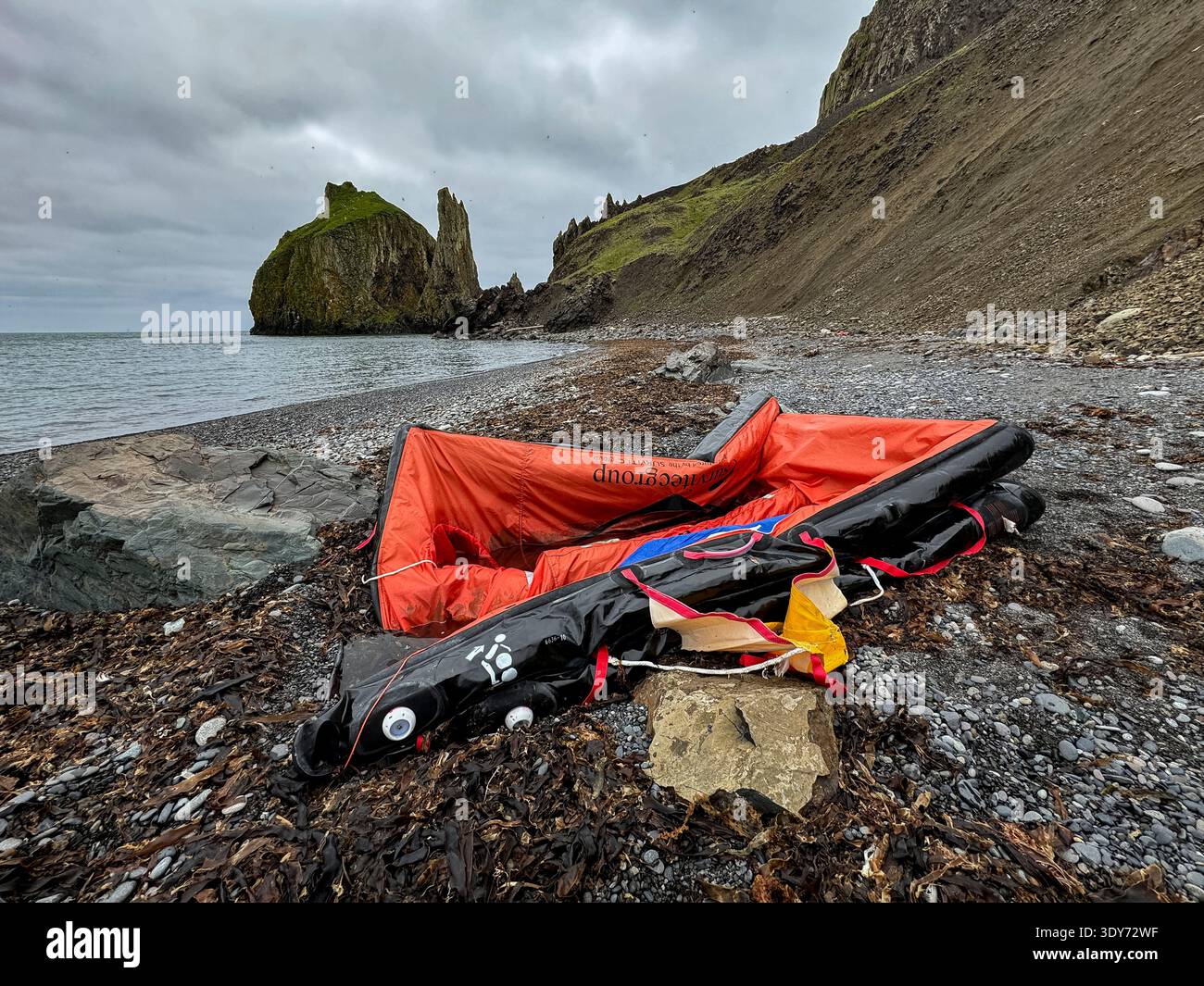 La zattera di salvataggio abbandonata si trova sulla spiaggia rocciosa vicino all'oceano sull'isola di Saint Mathew in Alaska sotto il cielo nuvoloso Foto Stock