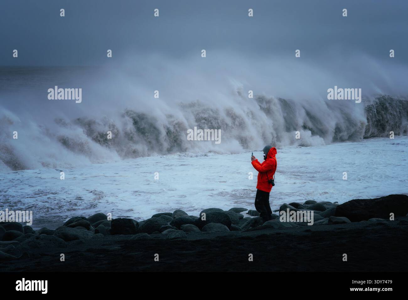 Man cattura le onde delle sneaker che si infrangono su rocce durante una tempesta in una spiaggia in Islanda Foto Stock