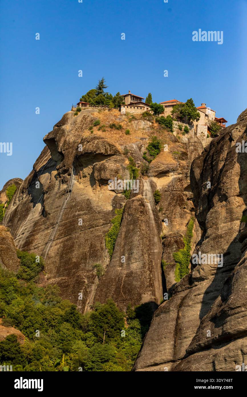 Il monastero è situato su una ripida parete rocciosa in Grecia, con aspre scogliere e vegetazione sparsa sotto un cielo azzurro Foto Stock