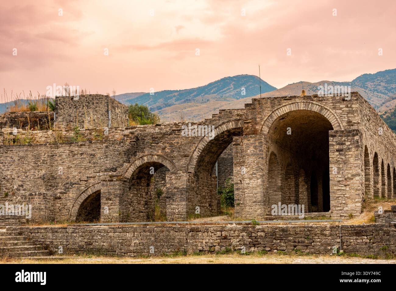 Vista al tramonto di archi in pietra al castello di Gjirokastr con montagne sullo sfondo e colori caldi nel cielo a Gjirokaster Albania Foto Stock