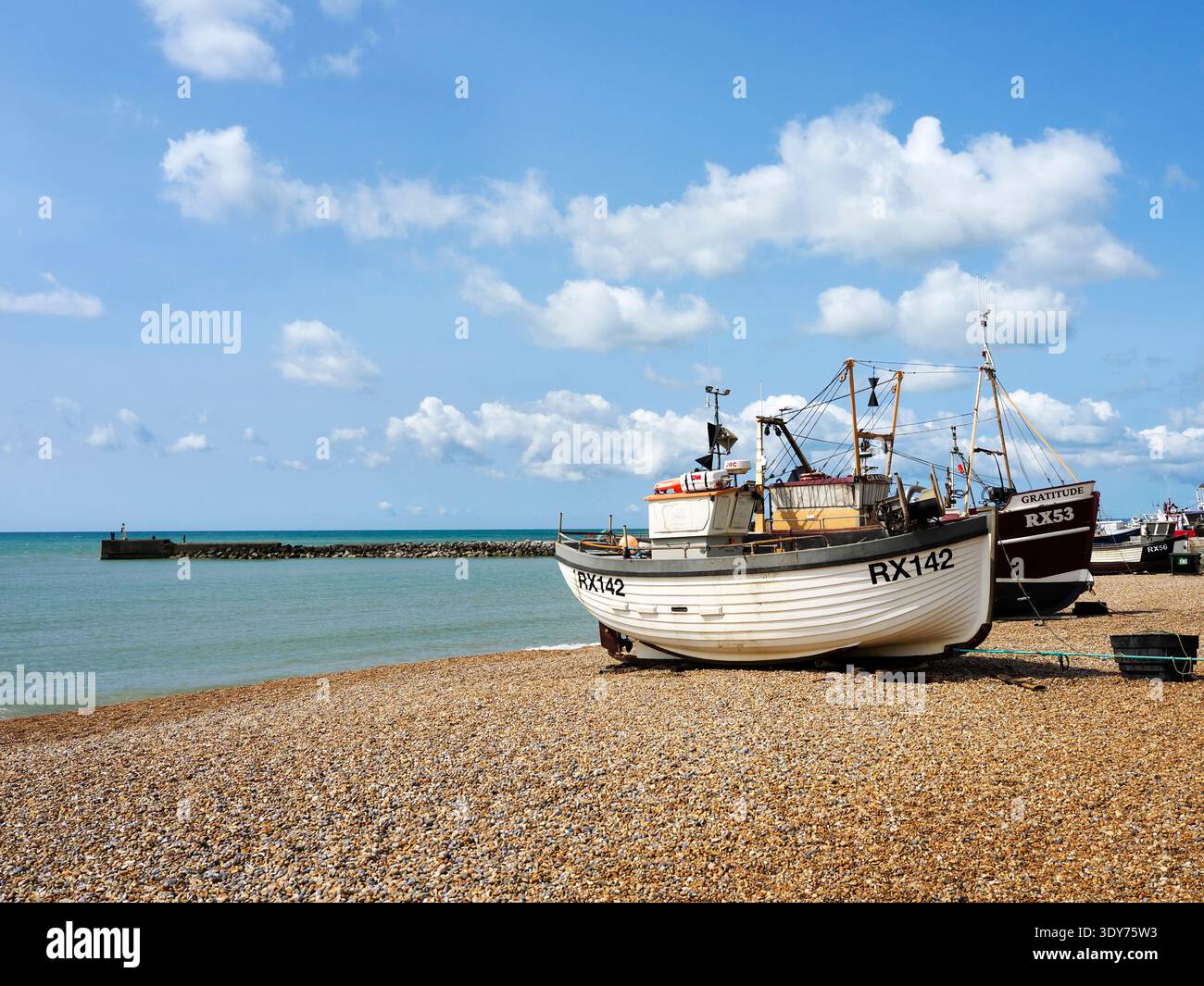 Barche che riposano sul ciottolo di Hastings con mare blu e nuvole in alto nell'East Sussex Foto Stock