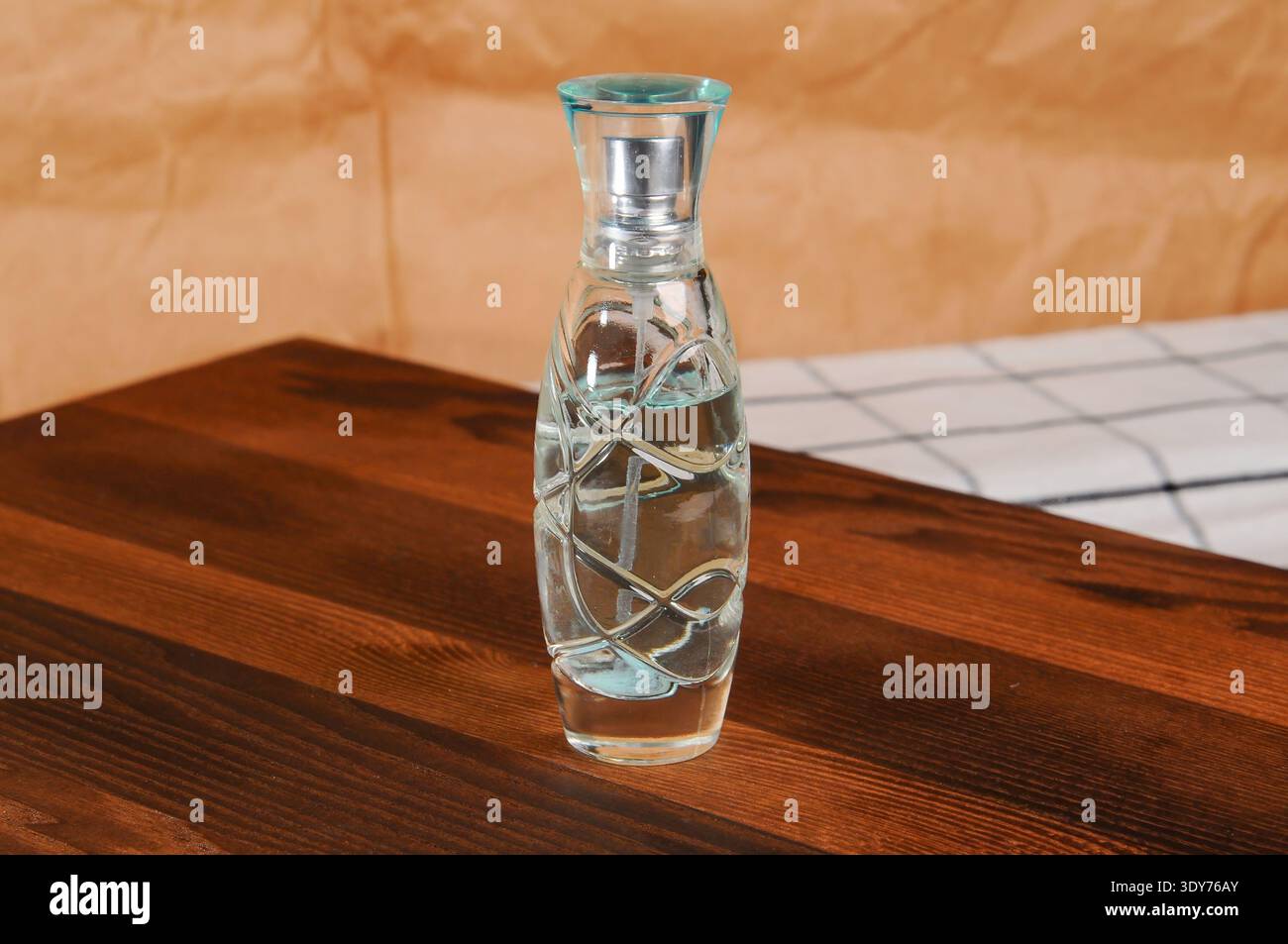 Una bottiglia di profumo in vetro con una superficie ruvida si trova su un tavolo in legno, pronto per l'uso Foto Stock