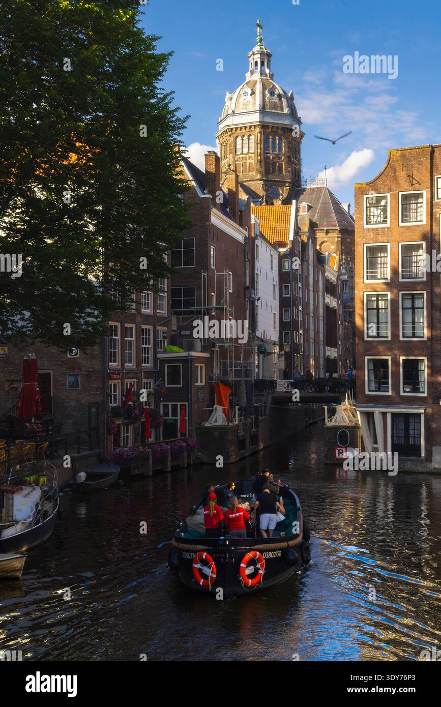 La barca naviga attraverso i canali di Amsterdam al tramonto vicino alla Basilica di San Nicola nell'Olanda settentrionale Foto Stock