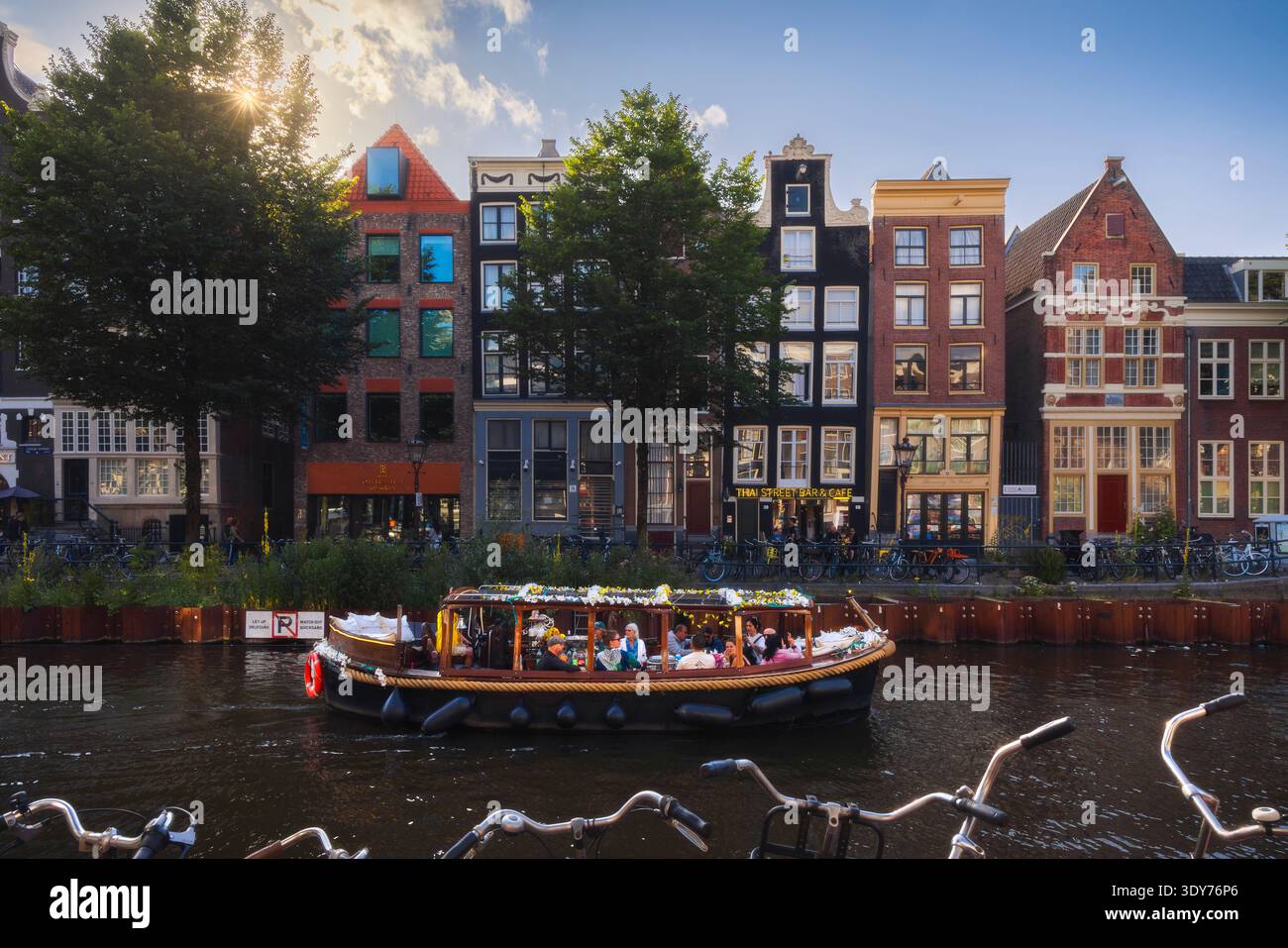 Canali di Amsterdam con una barca durante il tramonto nell'Olanda settentrionale che mostra case e alberi lungo l'acqua Foto Stock