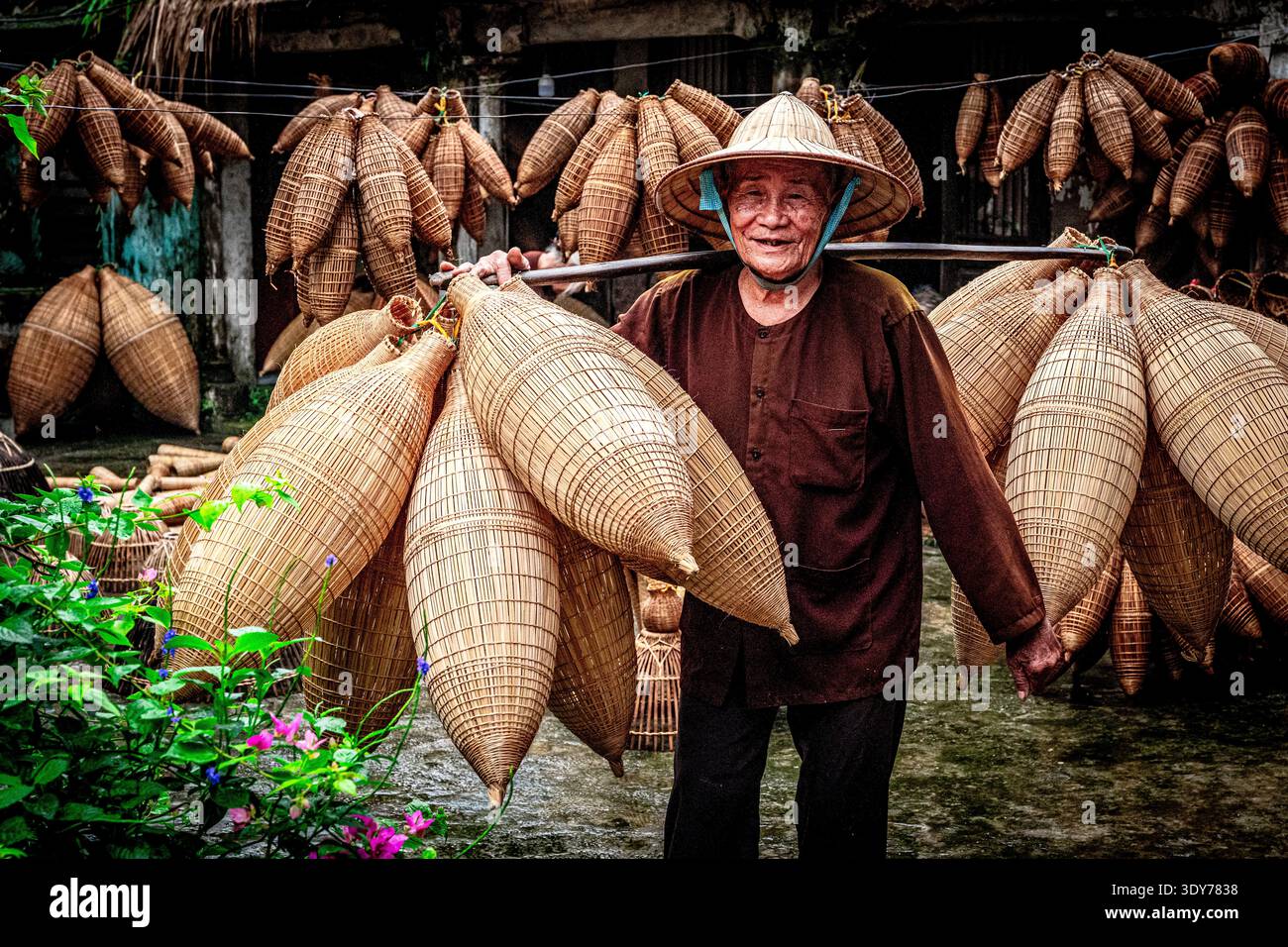L'uomo sorride mentre trasporta trappole per pesci fatte a mano ad Hanoi durante il giorno, mostrando un'artigianato locale e mezzi di sussistenza Foto Stock